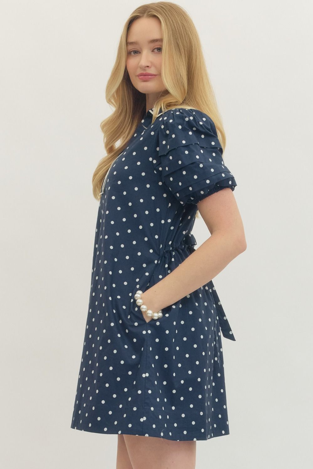 Woman wearing a navy blue dress with white polka dots on a plain background