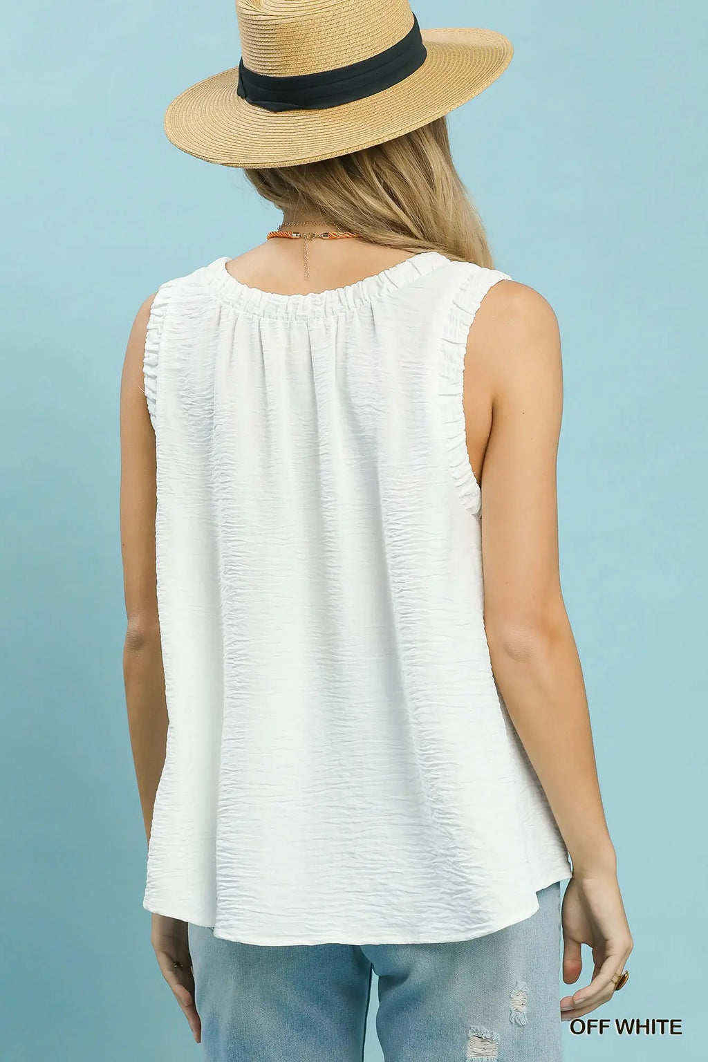 Person wearing a white sleeveless top and straw hat on a light blue background
