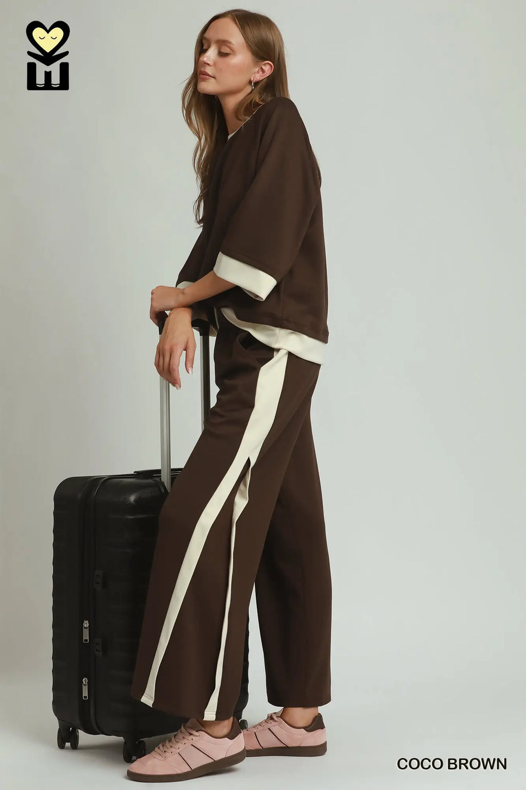 Woman in brown outfit with white stripes holding a suitcase on a plain background