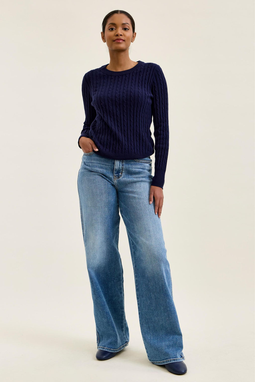 Woman wearing a navy sweater and blue jeans on a plain background