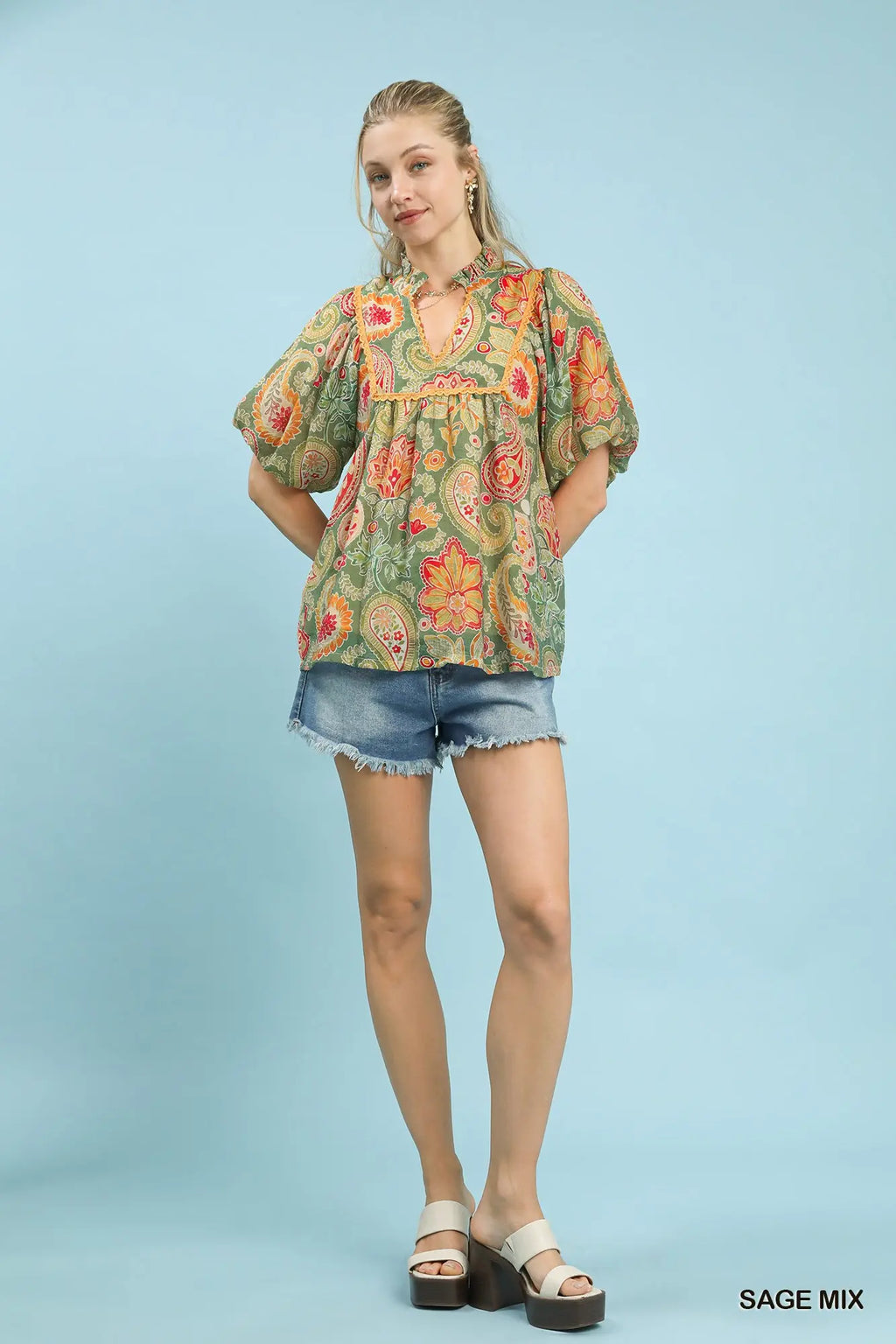 Woman wearing a floral blouse and denim shorts on a light blue background
