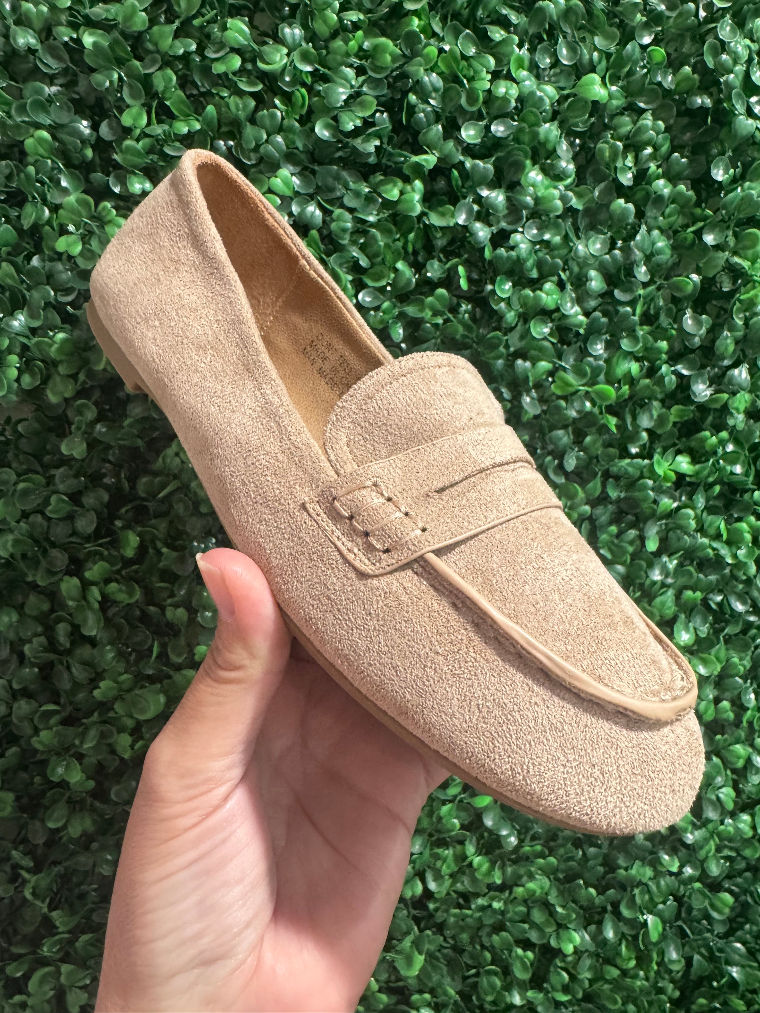 Beige loafer shoe held in a hand against a green grass background