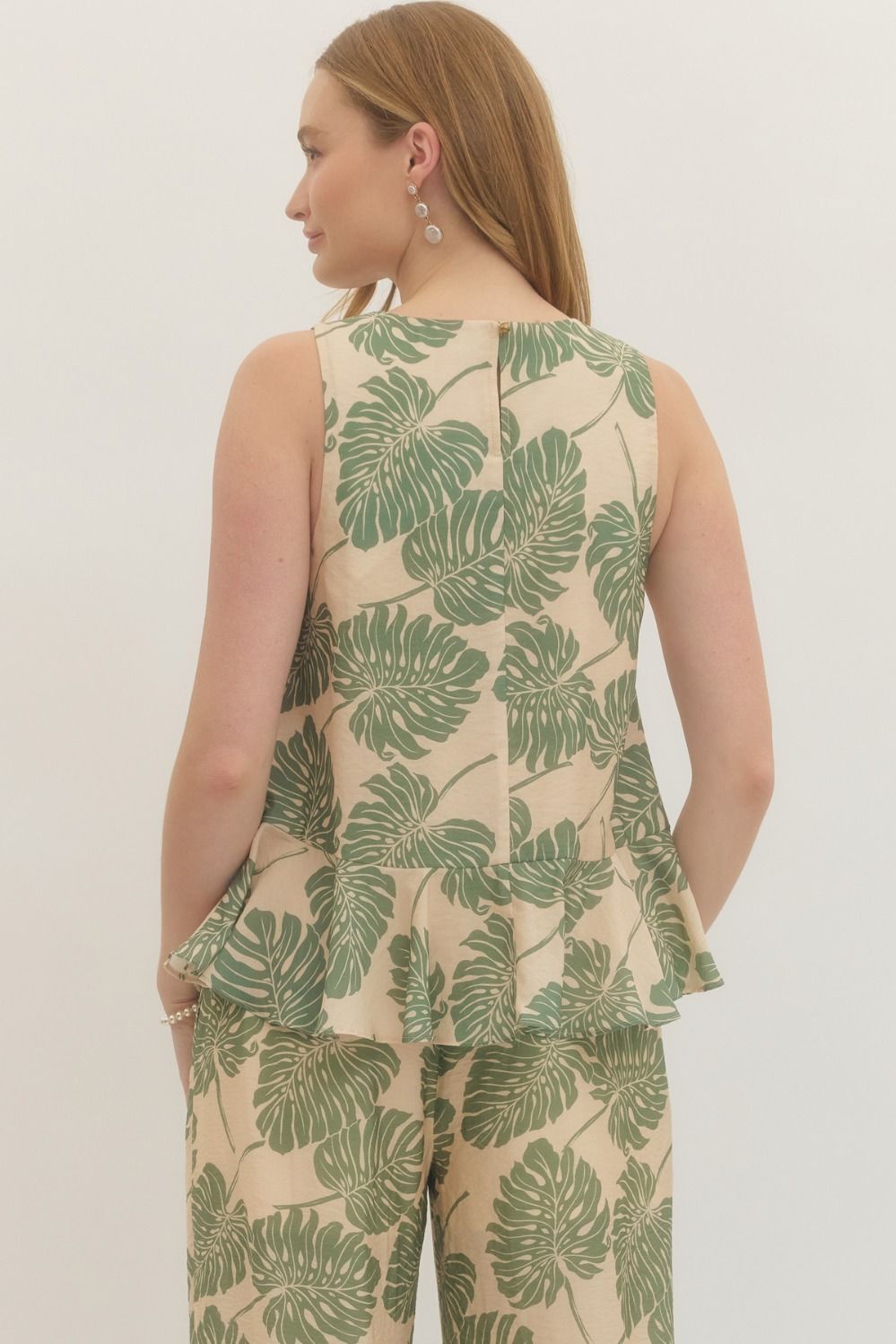 Woman wearing a sleeveless top and pants with green leaf pattern on a plain background