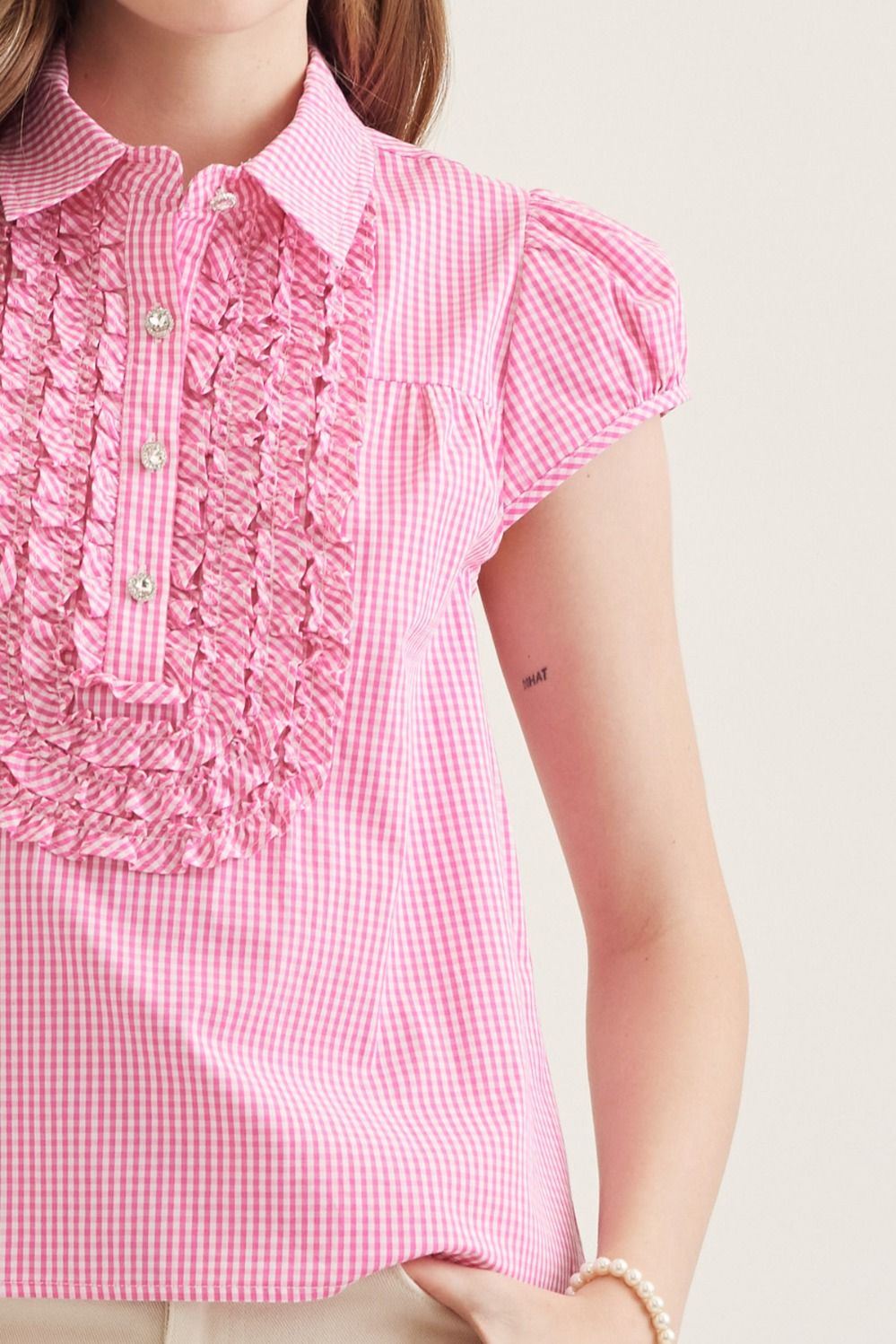 Close-up of a person wearing a pink checkered blouse with ruffled details.