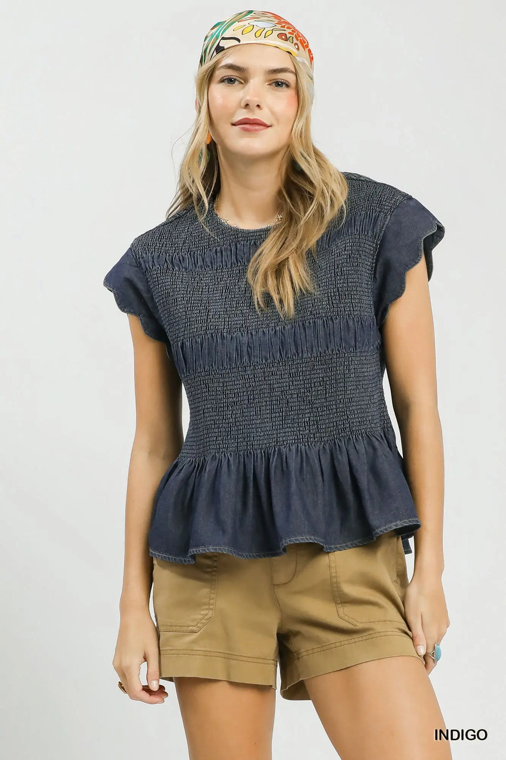 Woman wearing a dark blue peplum top and beige shorts with a colorful headband on a light gray background.