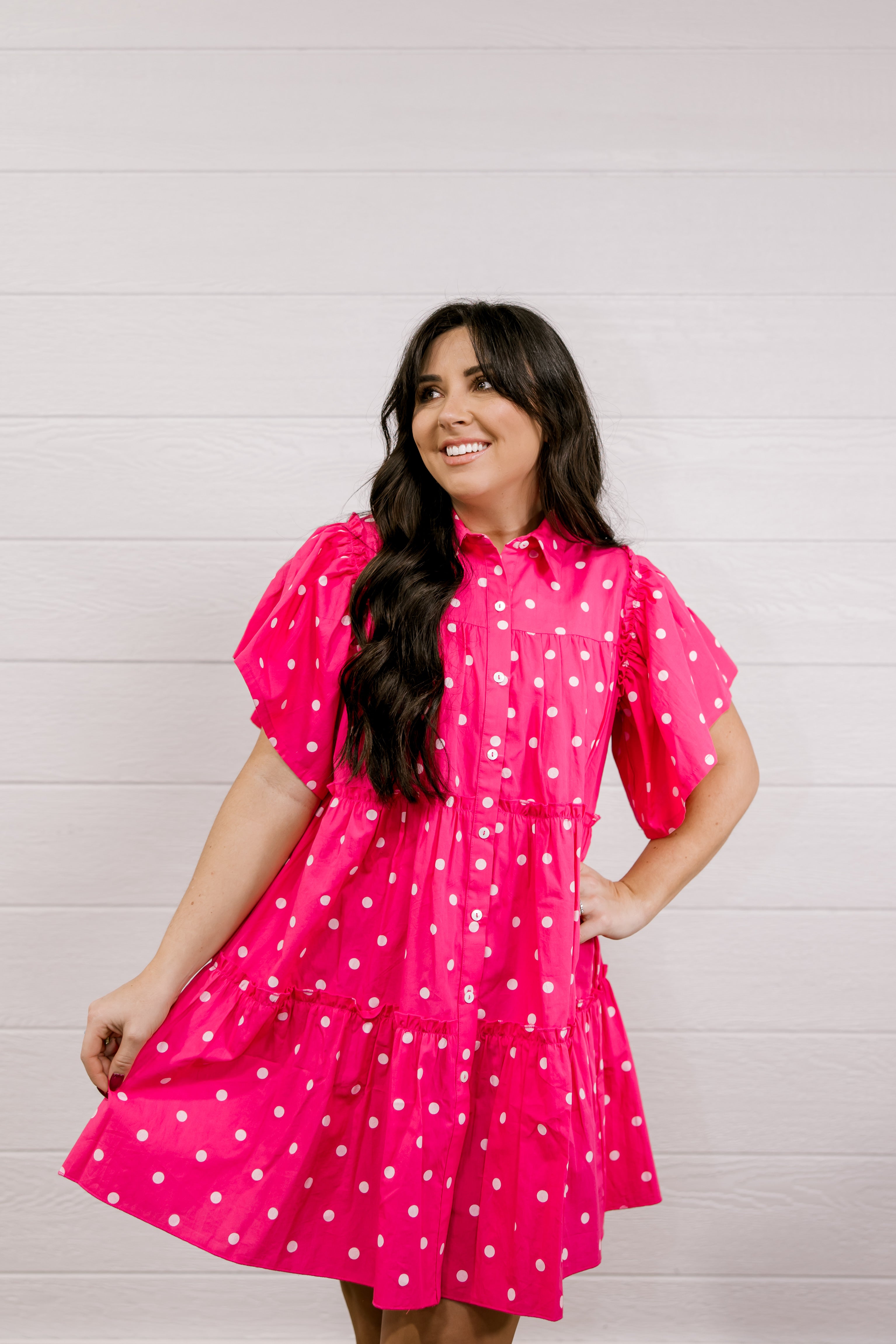 Woman wearing a pink polka dot dress against a light wooden panel background