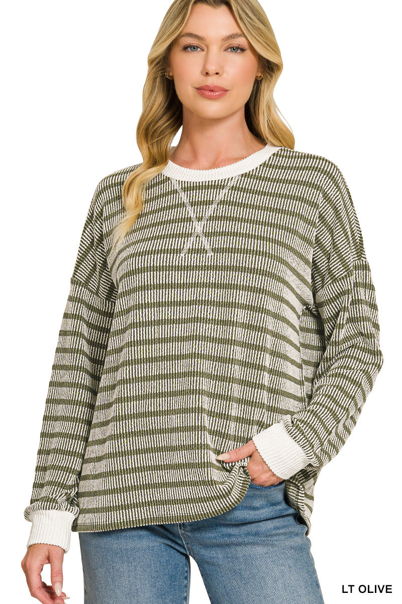 A woman modeling a long-sleeve knit sweater with horizontal olive green and cream stripes, featuring a cream crew neck and cuffs, paired with blue jeans against a white background.