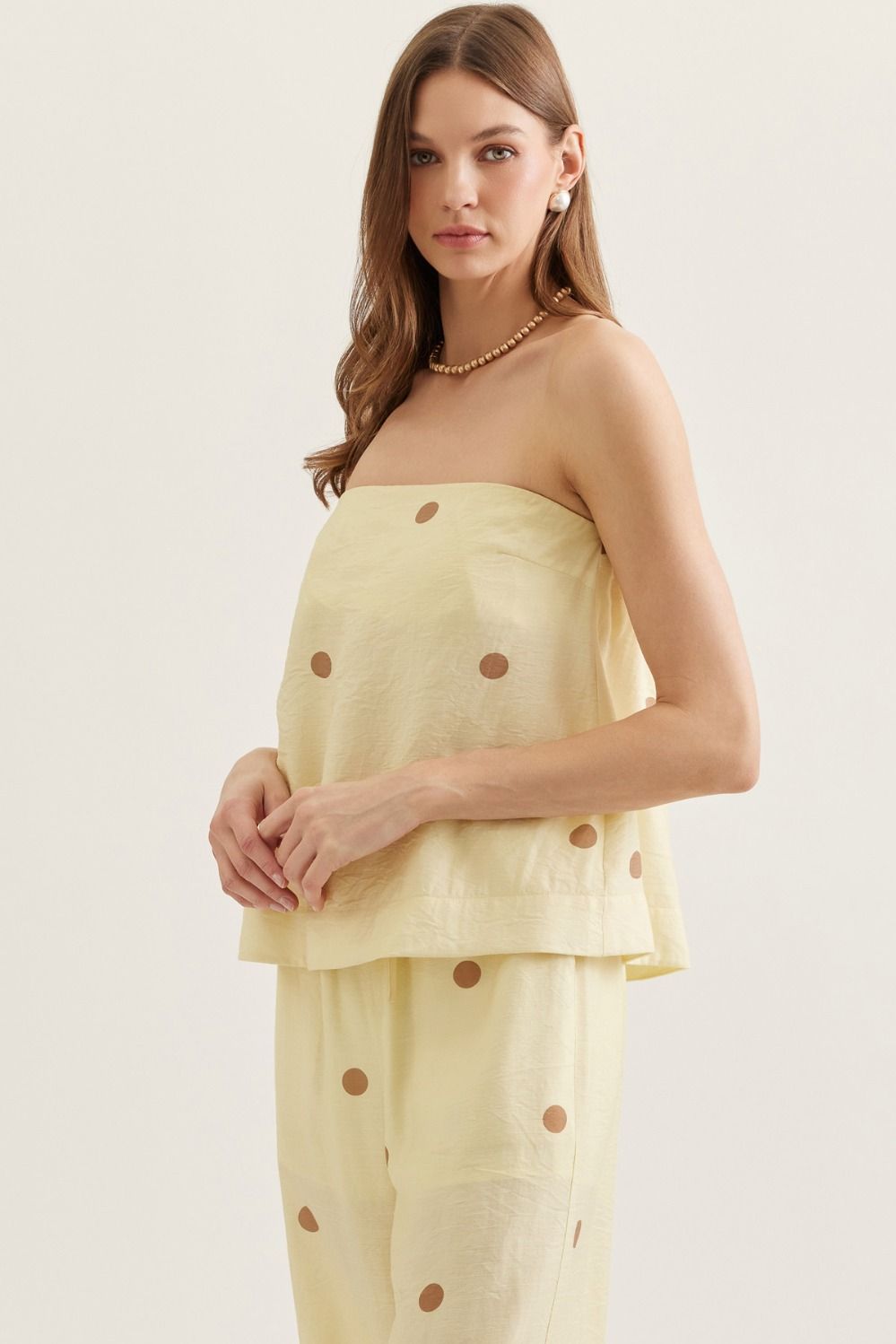 Woman wearing a light yellow strapless top and pants with brown polka dots on a white background