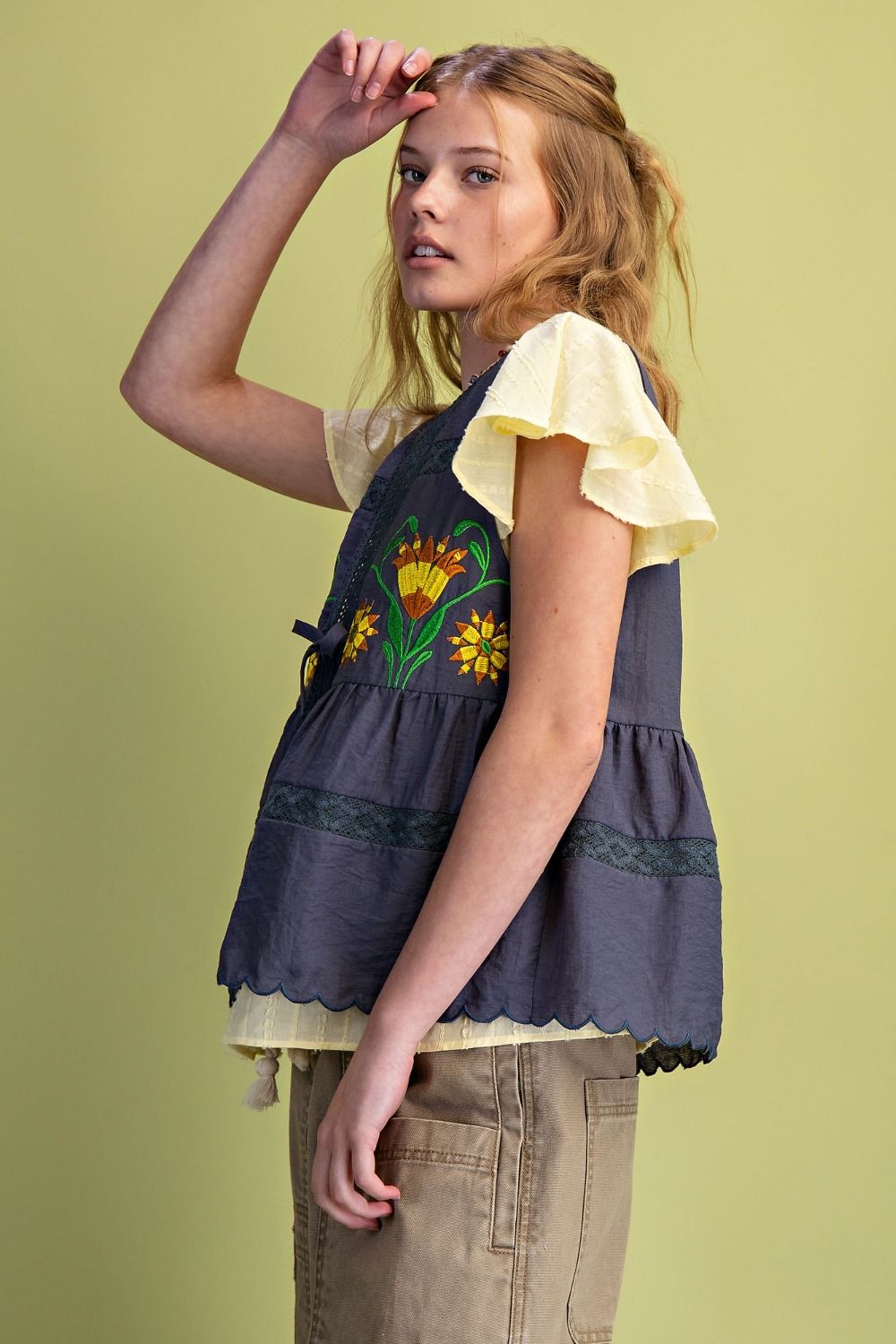 Young girl wearing a navy blue top with floral embroidery on a light green background