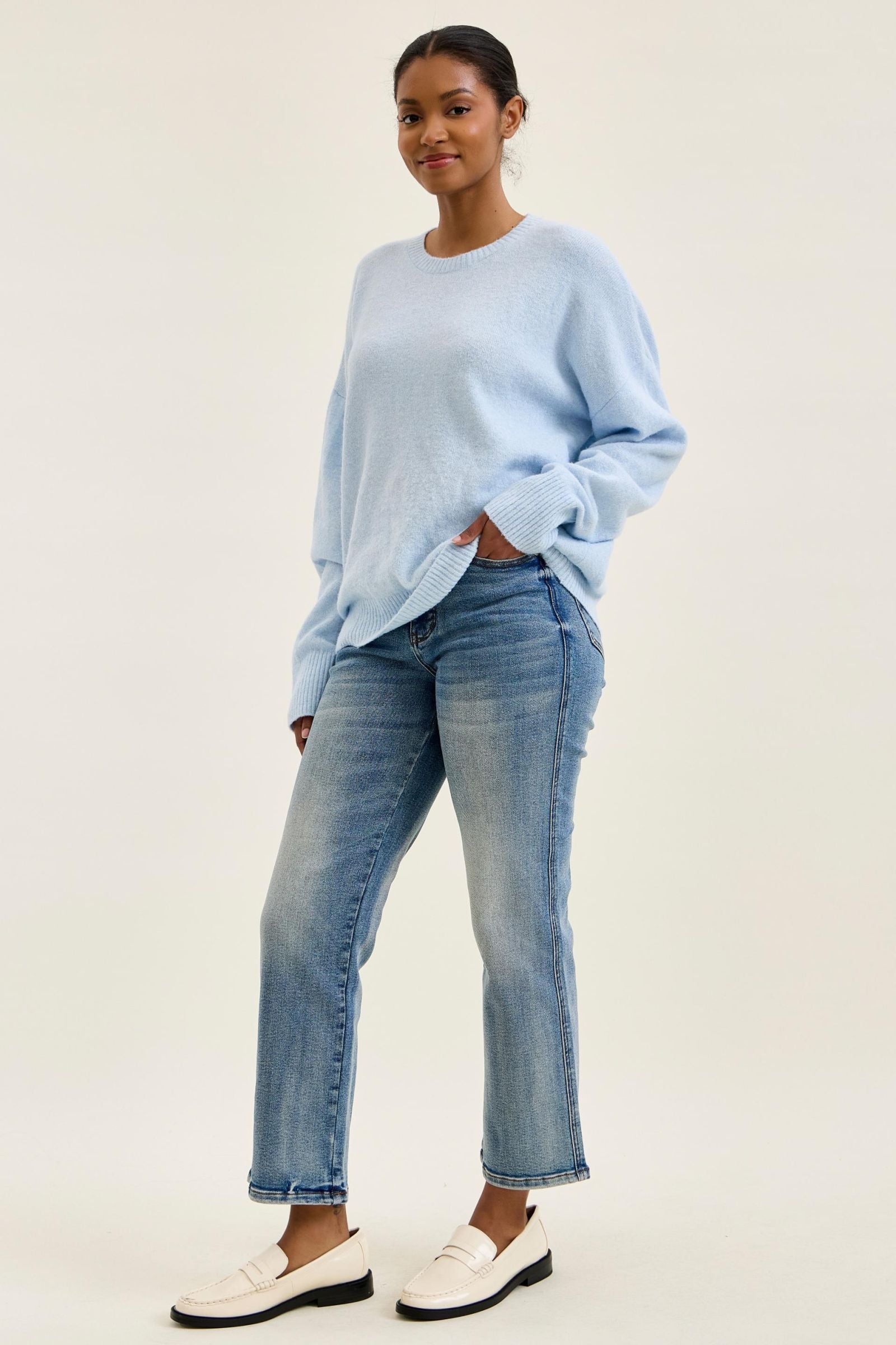 Woman wearing a light blue sweater and jeans on a plain background