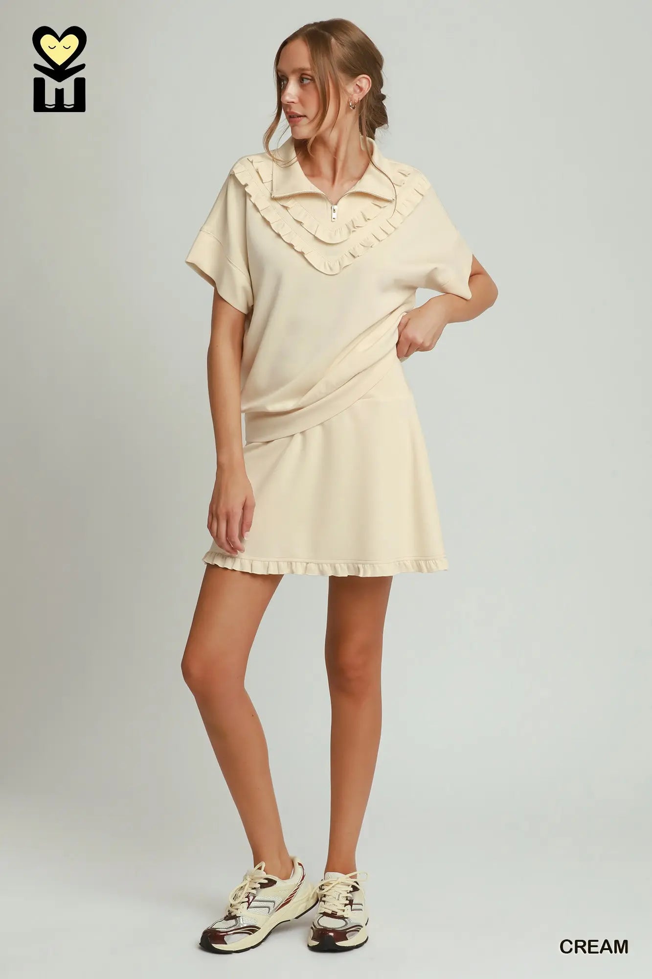 Woman wearing a cream-colored set with ruffled details on a plain background