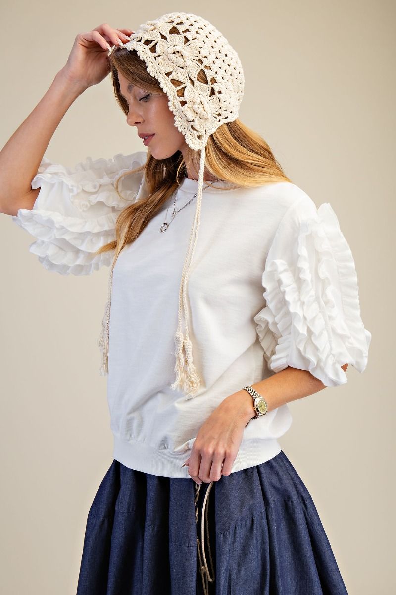 Woman wearing a white blouse with ruffled sleeves and a lace bonnet against a beige background