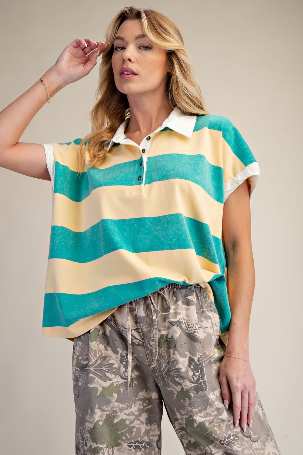 Woman wearing a yellow and teal striped shirt with camouflage pants on a beige background