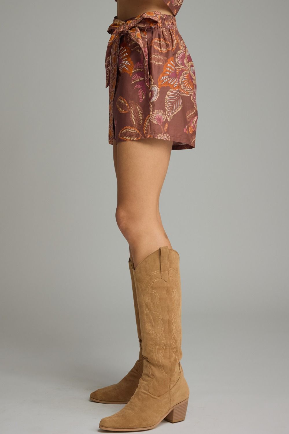 Person wearing brown knee-high boots and patterned shorts on a gray background
