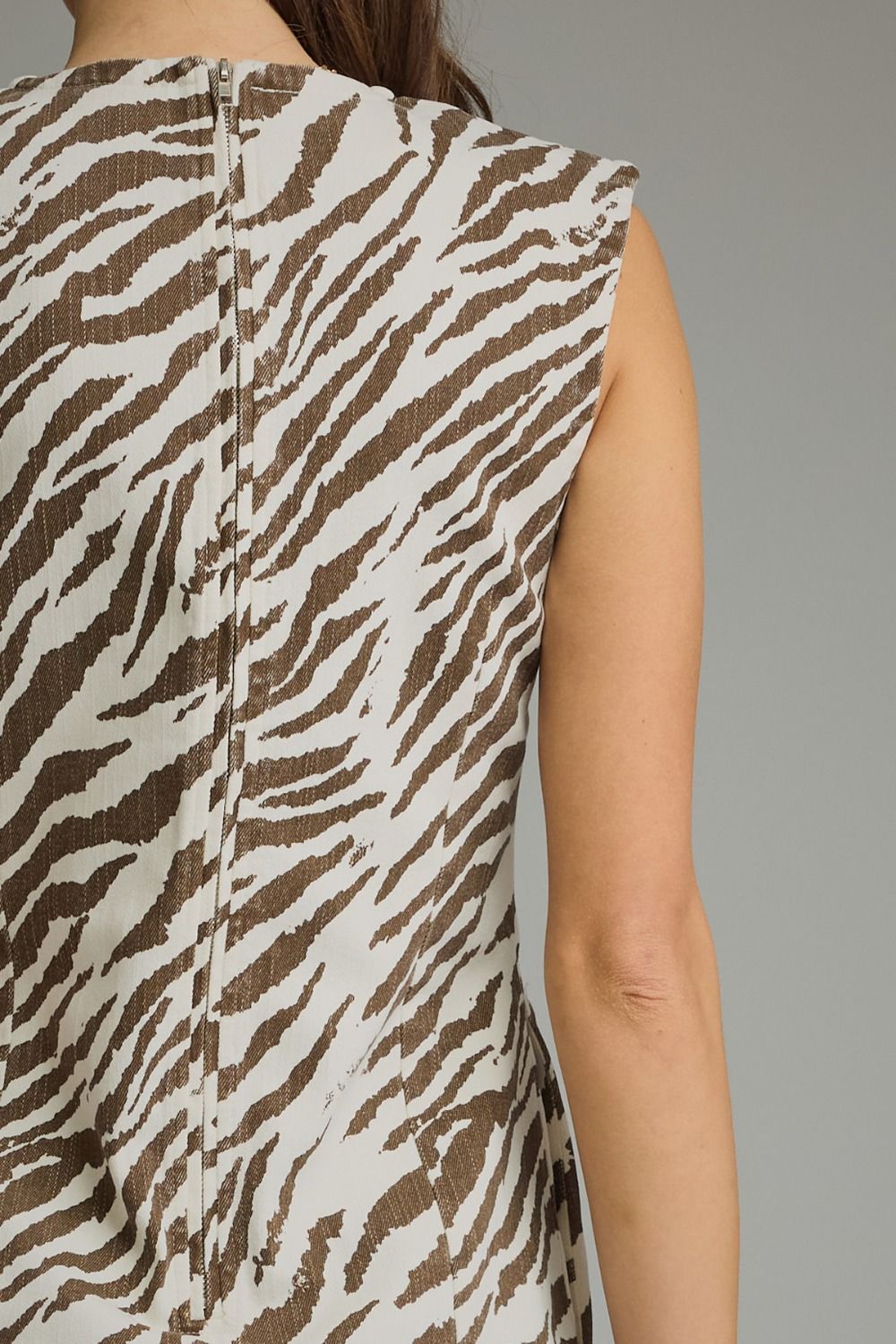 Close-up back view of a sleeveless top with a brown and off-white zebra print pattern, shown on a model against a plain gray background.