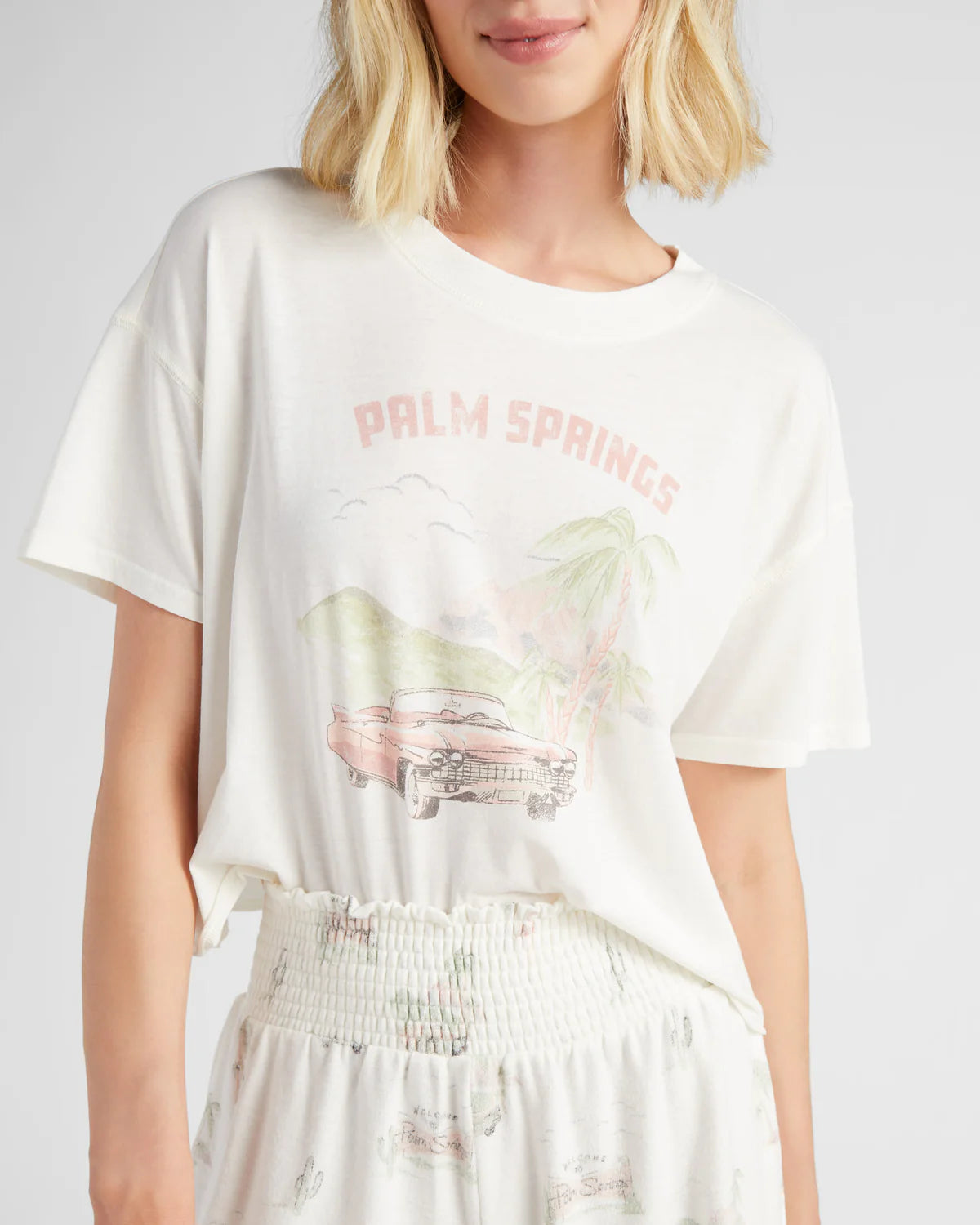 Person wearing a white t-shirt with 'Palm Springs' graphic design on a plain background