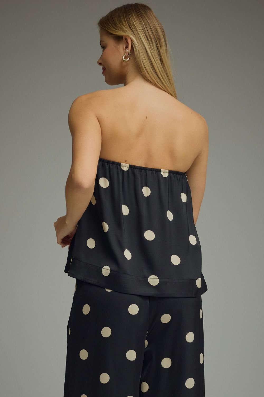 Woman wearing a black strapless top and pants with white polka dots on a gray background