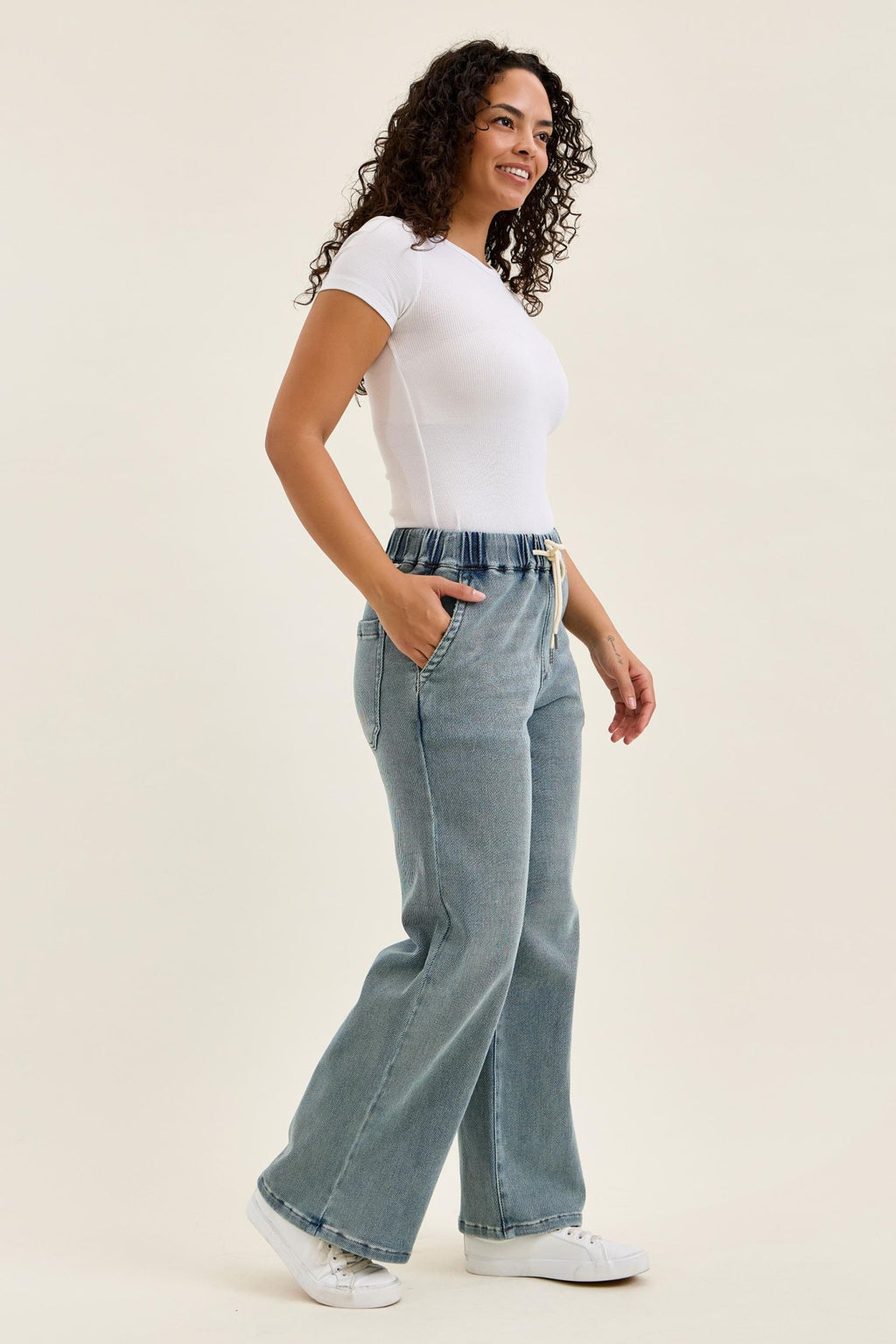 Woman wearing a white t-shirt and light blue jeans on a beige background