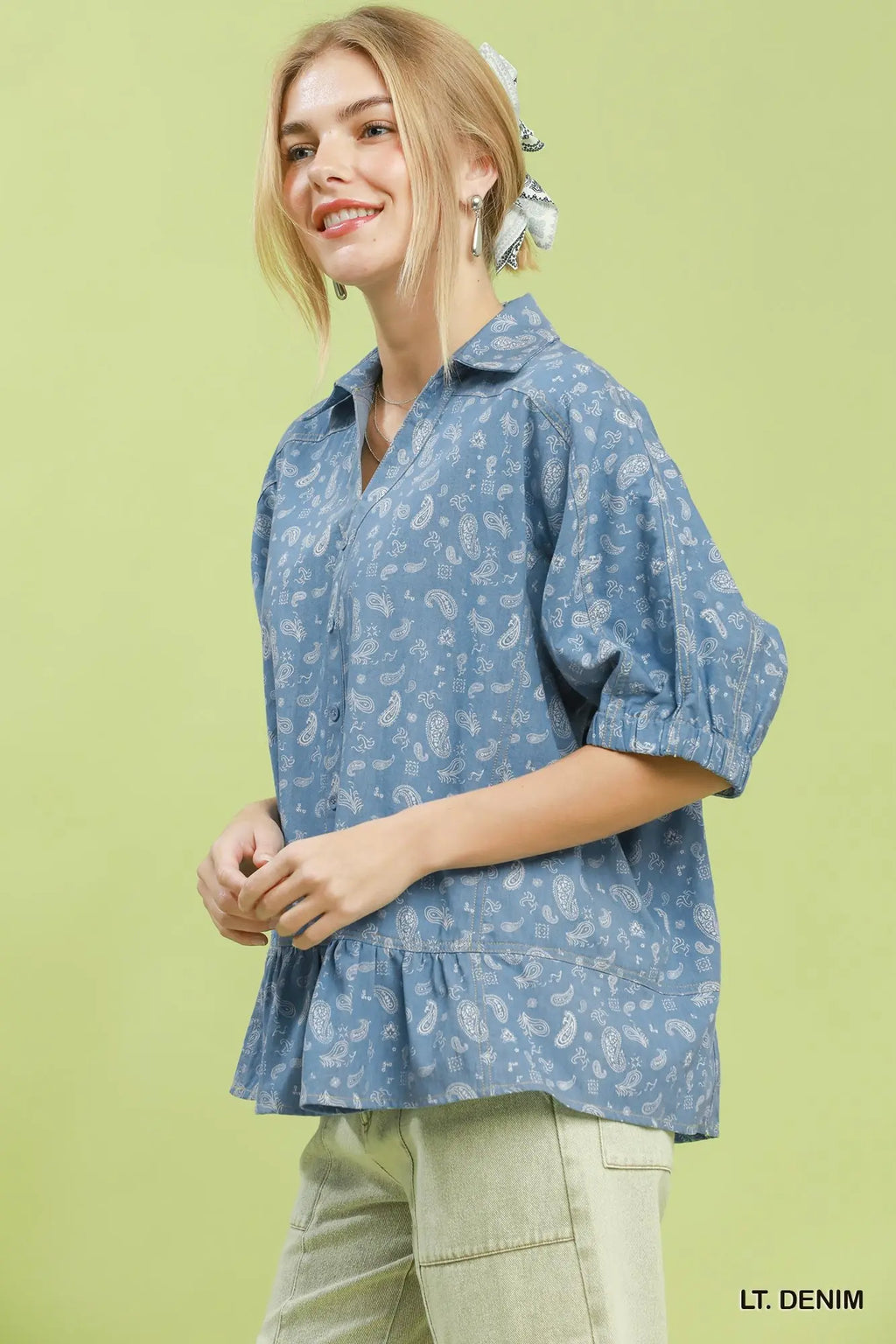 Woman wearing a light denim shirt with a subtle pattern on a green background