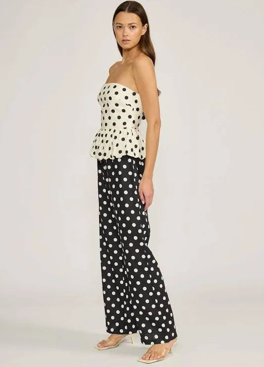 Woman wearing a polka dot strapless top and wide-leg pants on a white background