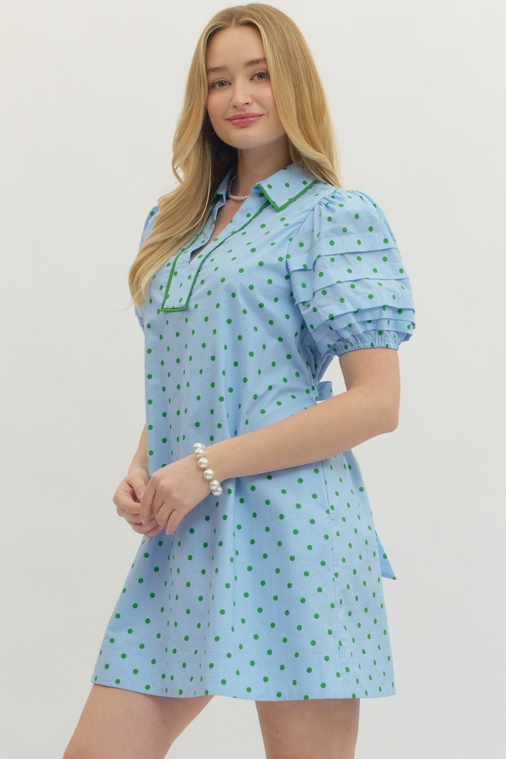 Woman wearing a light blue dress with green polka dots on a plain background