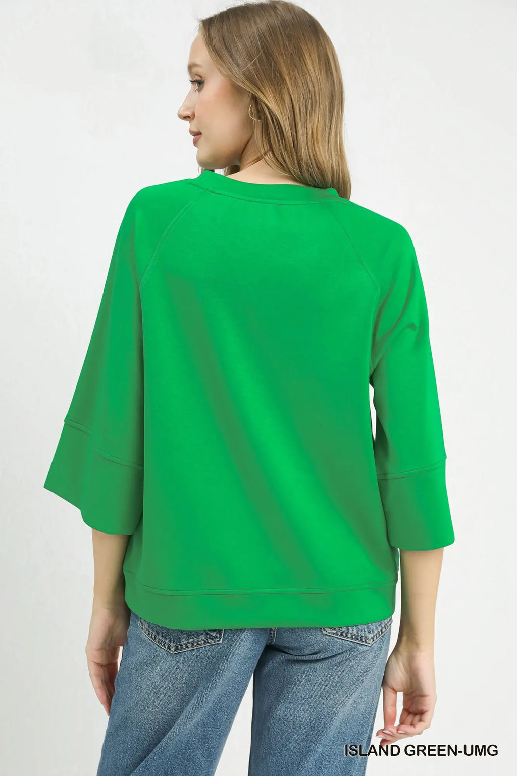 A woman shown from the back wearing a bright green three-quarter sleeve top and blue jeans against a plain white background.