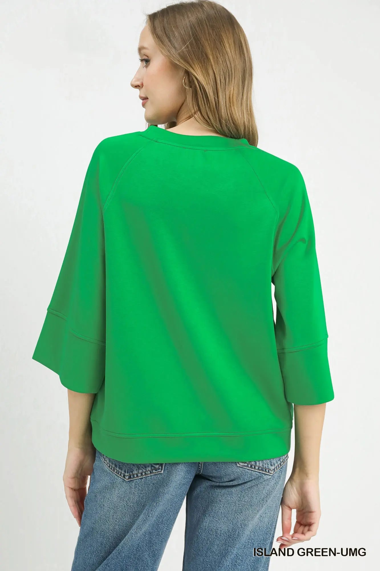 A woman shown from the back wearing a bright green three-quarter sleeve top and blue jeans against a plain white background.