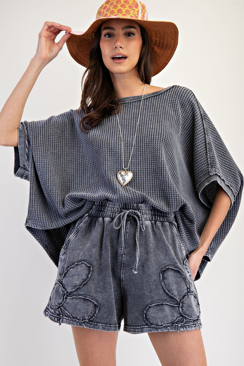 Woman wearing a gray oversized top and denim shorts with a sun hat on a white background