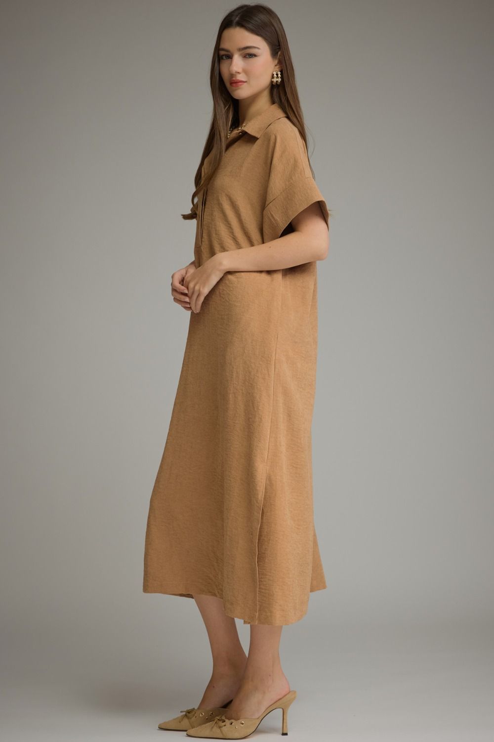 A woman modeling a tan short-sleeve midi dress with a collared neckline, shown against a neutral gray studio background.