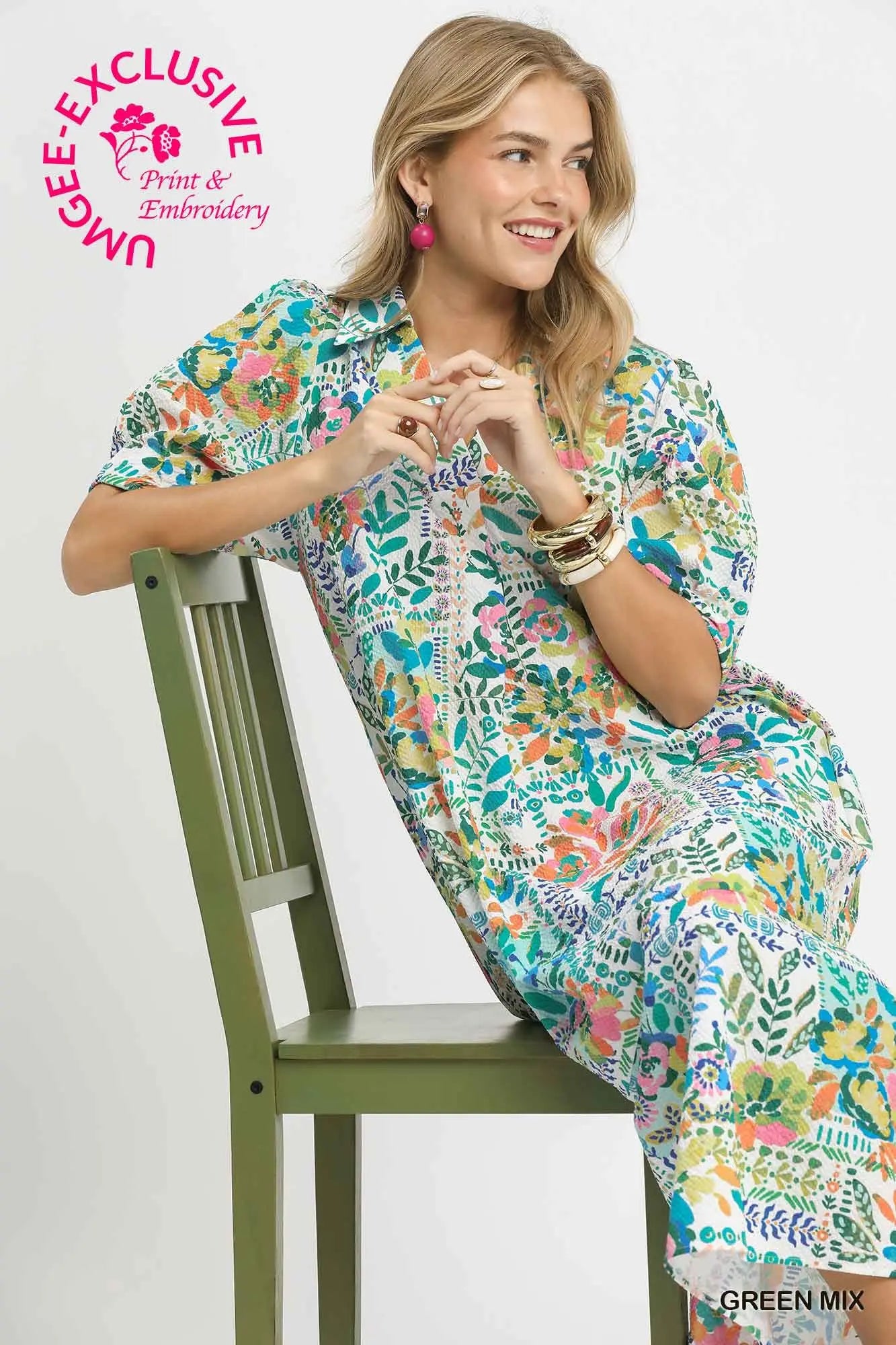 Woman sitting on a chair wearing a colorful floral dress with 'UMgee Exclusive' branding.