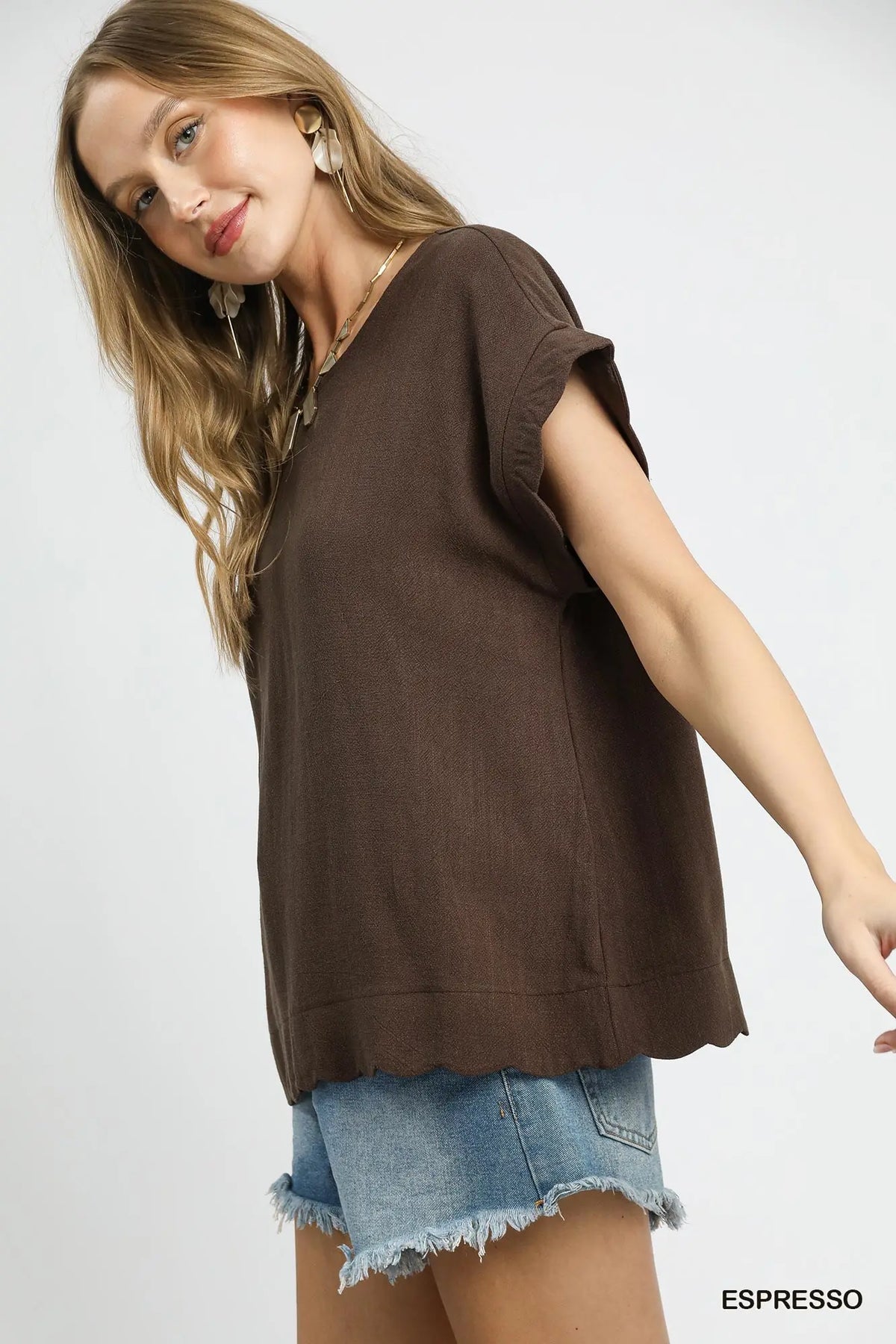 A woman wearing a brown short-sleeve top with a scalloped hem and light blue denim shorts, photographed against a plain light background. The word 'ESPRESSO' appears in the bottom right corner.