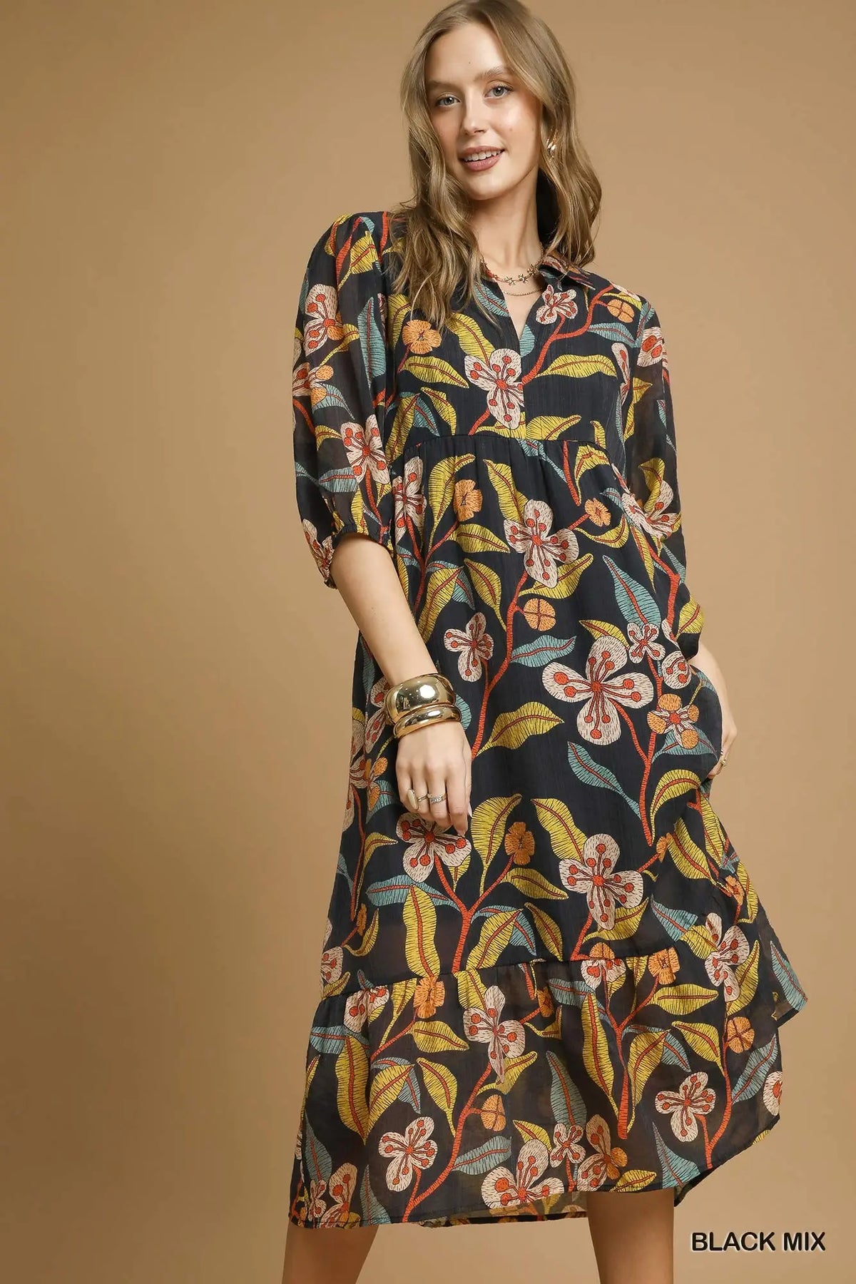 A woman models a black midi dress with a vibrant floral print in orange, yellow, and green, set against a solid tan studio background. The text 'BLACK MIX' is visible in the bottom right corner.