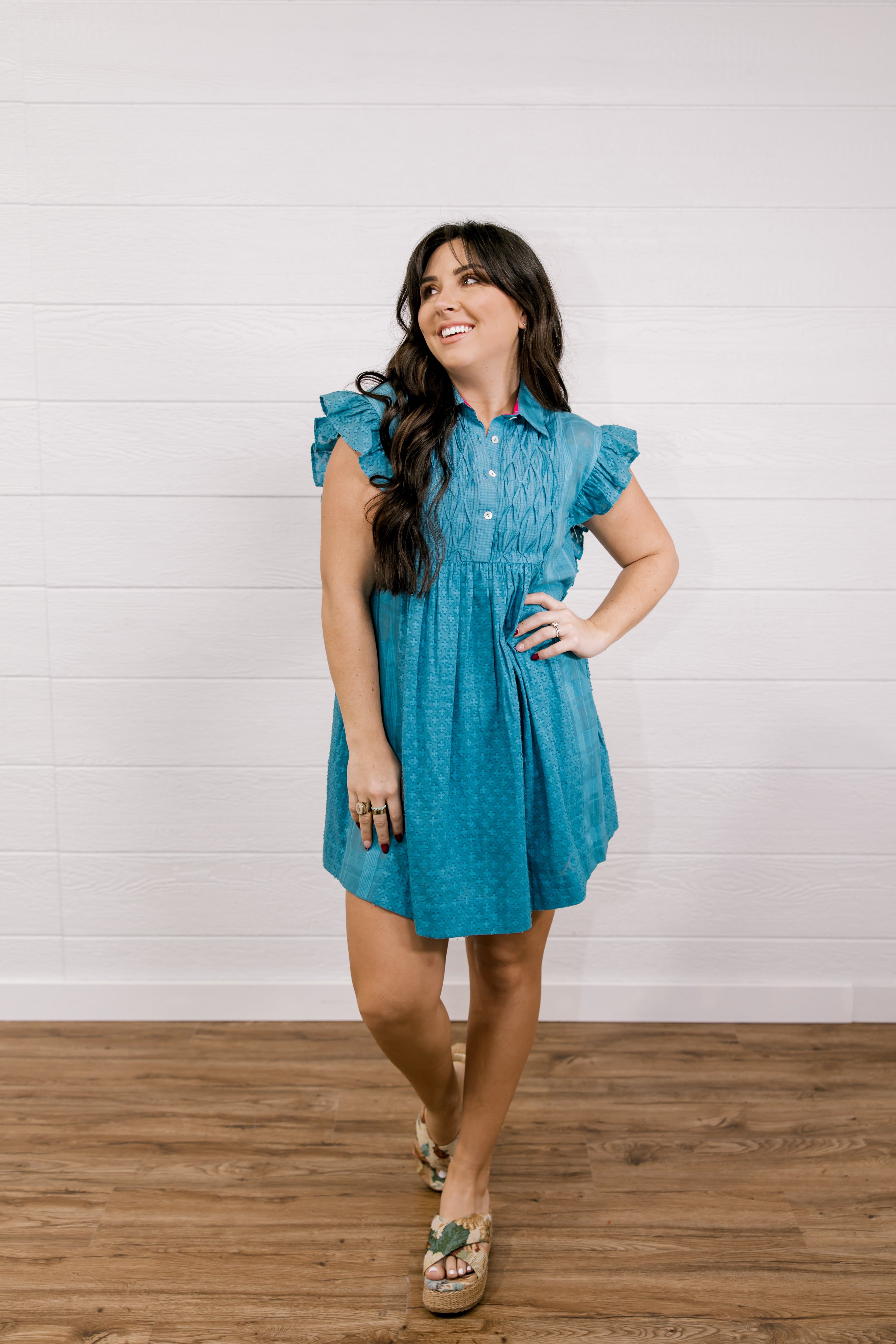 Woman wearing a blue dress standing on a wooden floor with a white wall background