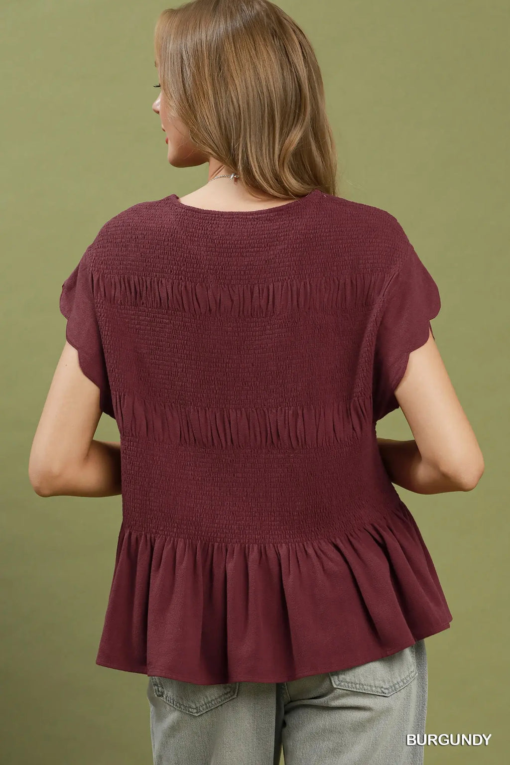 Woman wearing a burgundy top with fringes on a green background