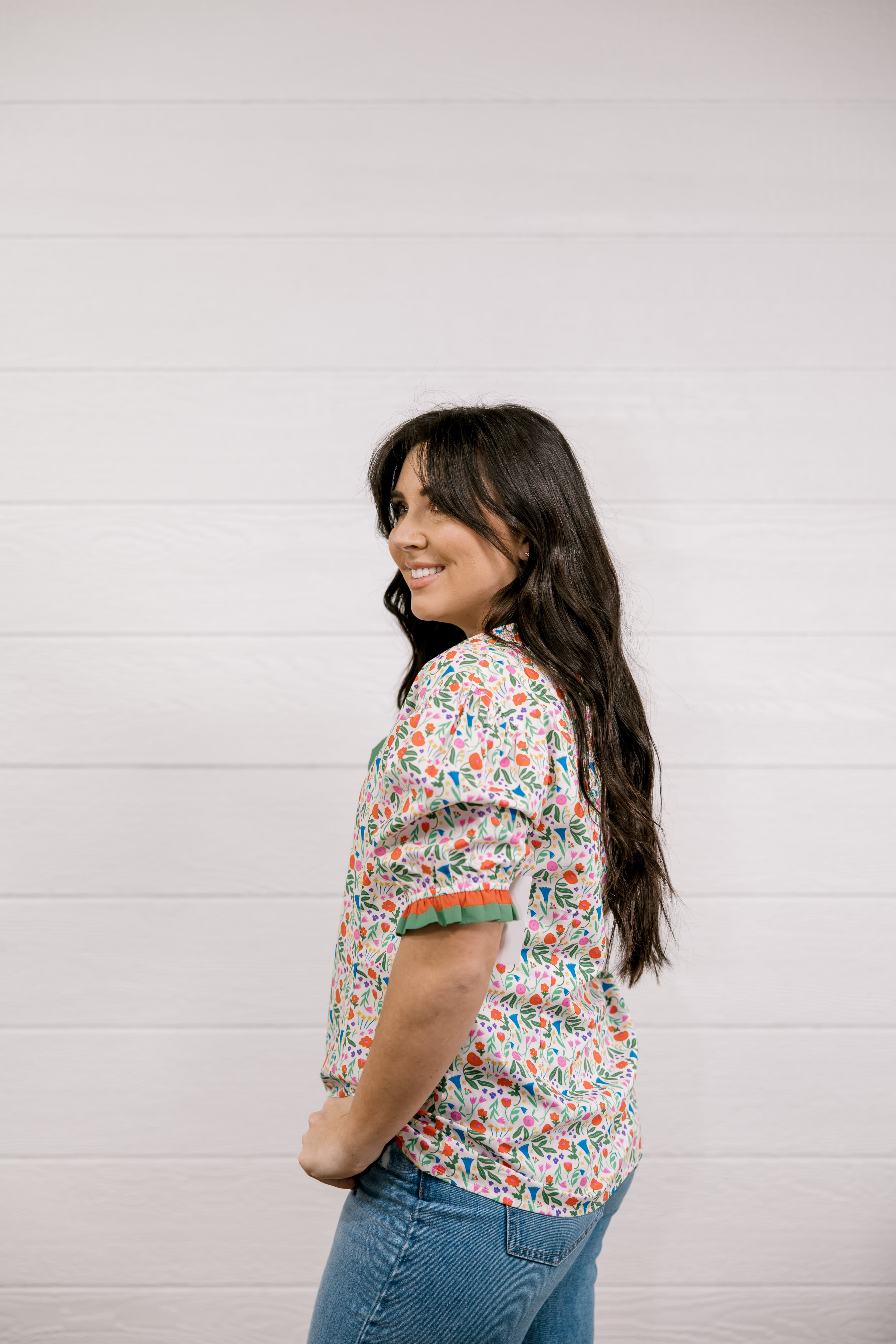 Woman wearing a floral blouse and jeans against a white background