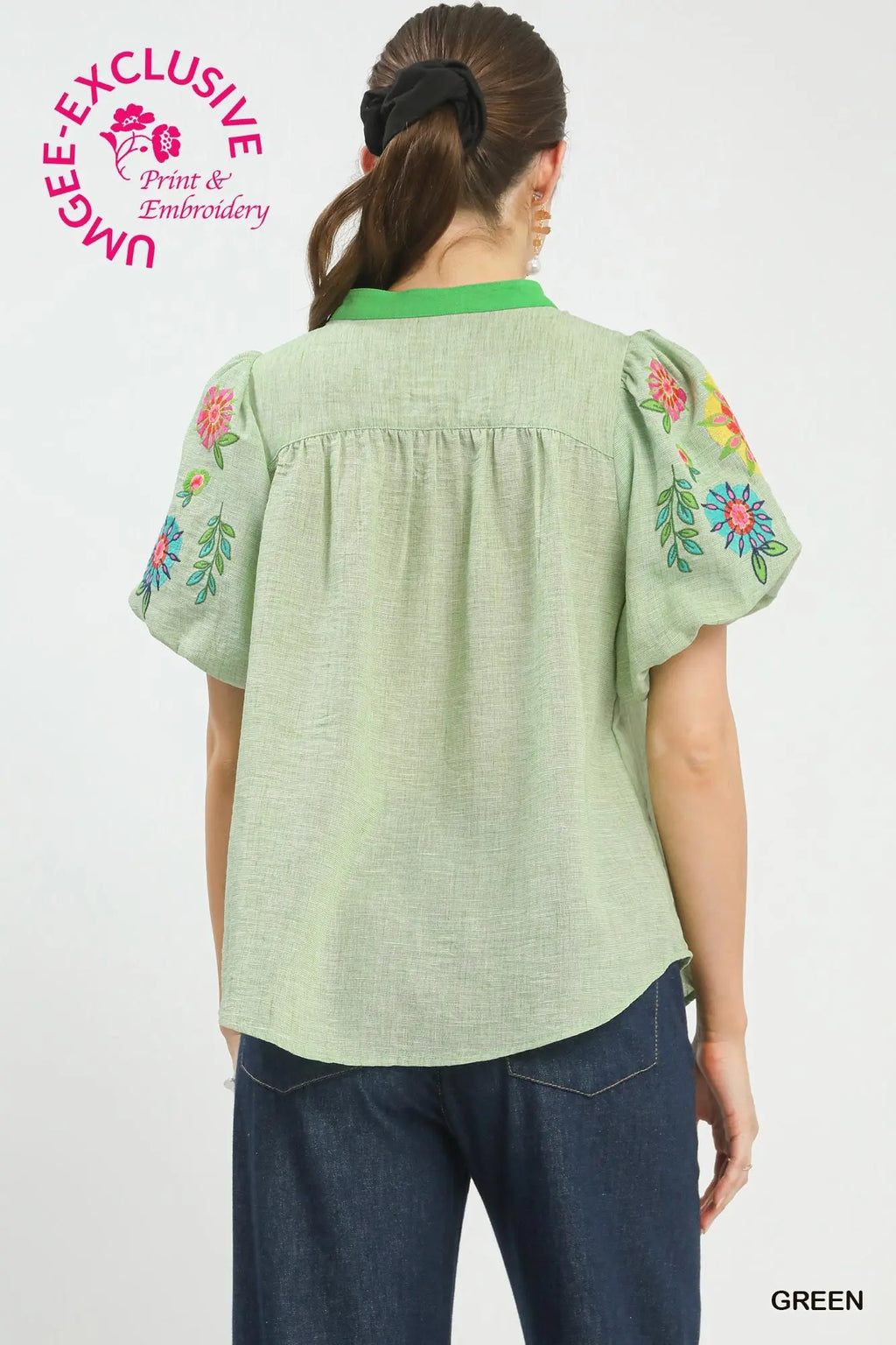 Green blouse with floral embroidery on sleeves worn by a person, against a white background.
