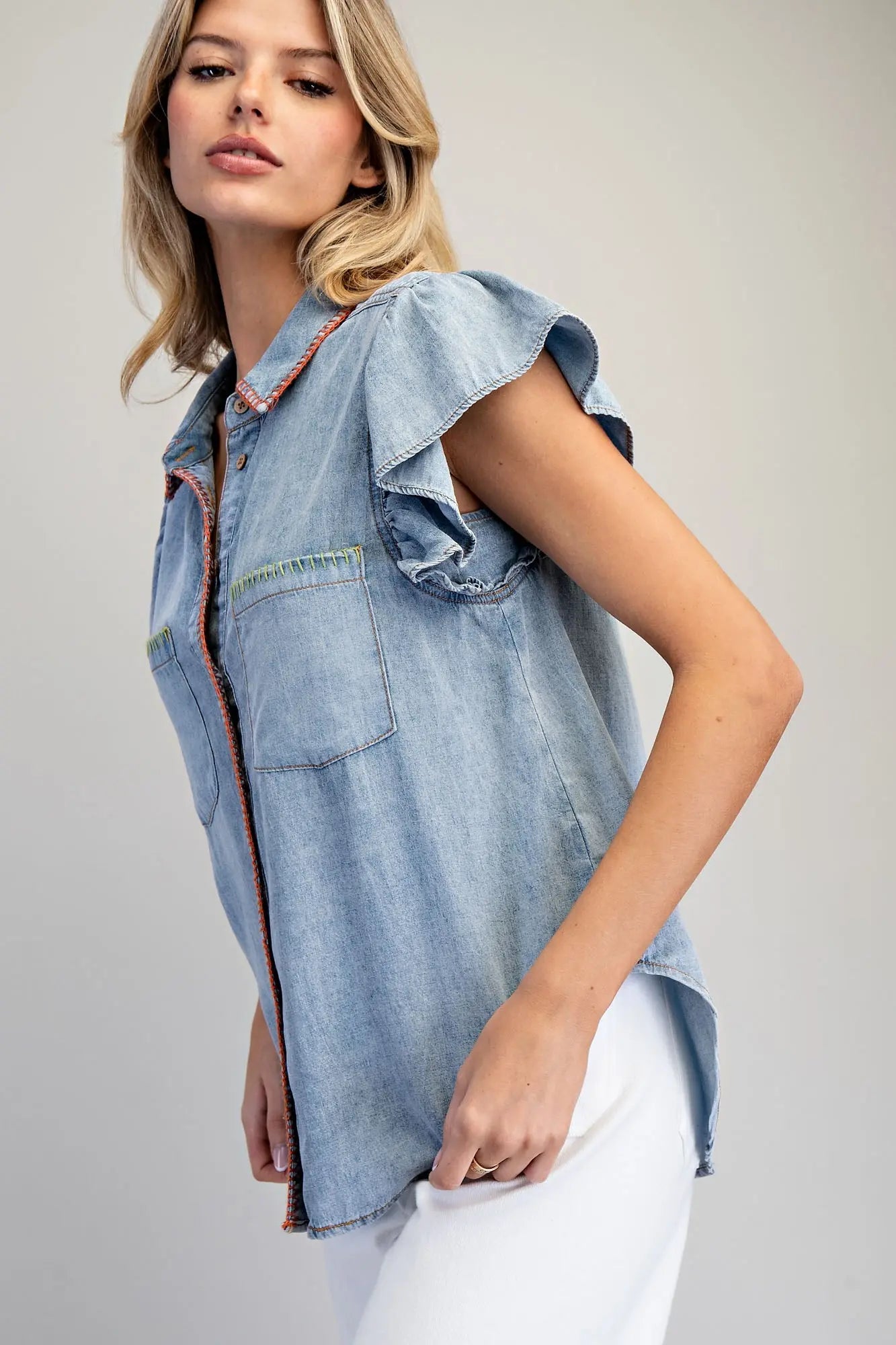Woman wearing a light blue denim top with ruffled sleeves on a gray background