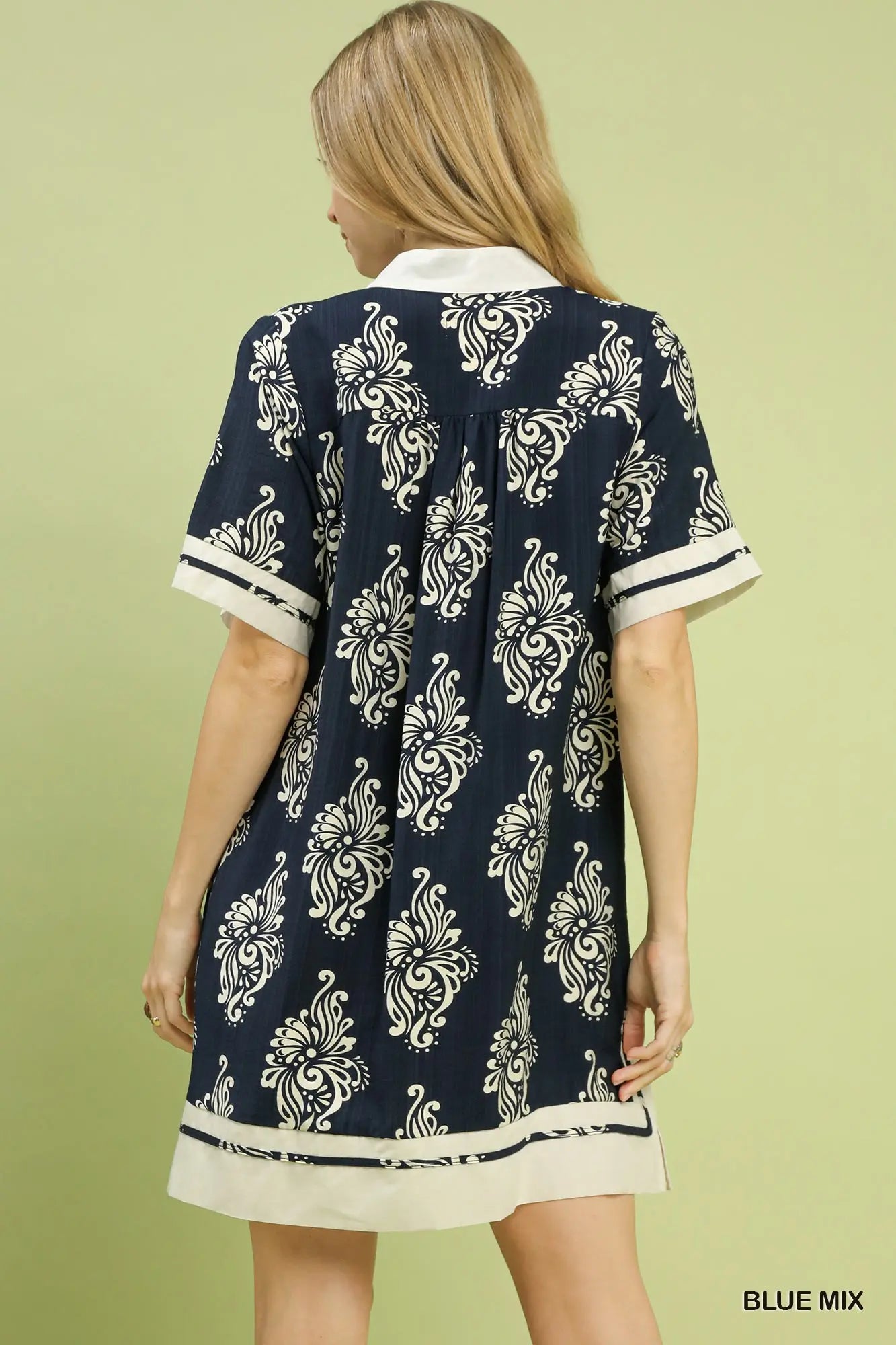 Woman wearing a navy blue dress with white pattern on a light green background
