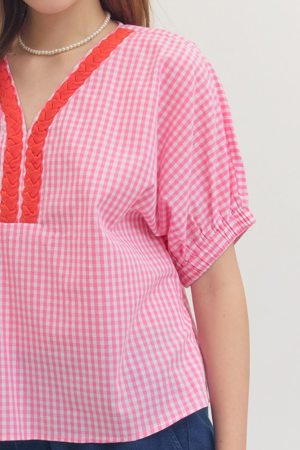 Person wearing a pink and red checkered top with a plain background