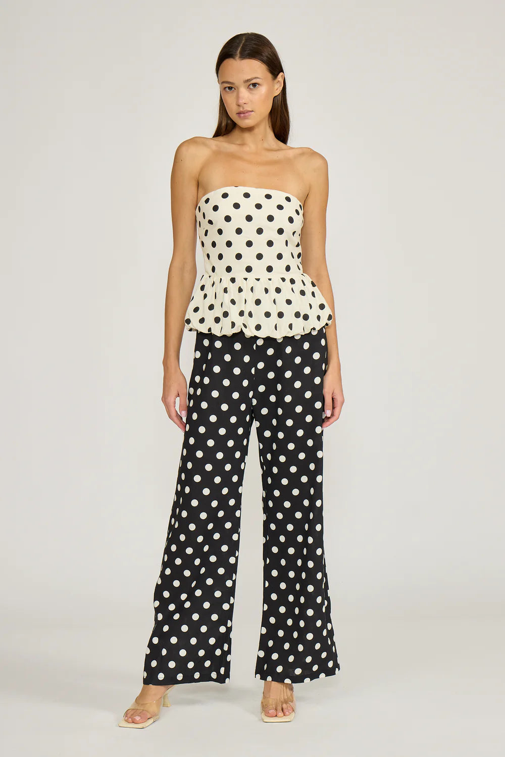 Woman wearing a polka dot strapless top and wide-leg pants on a plain background