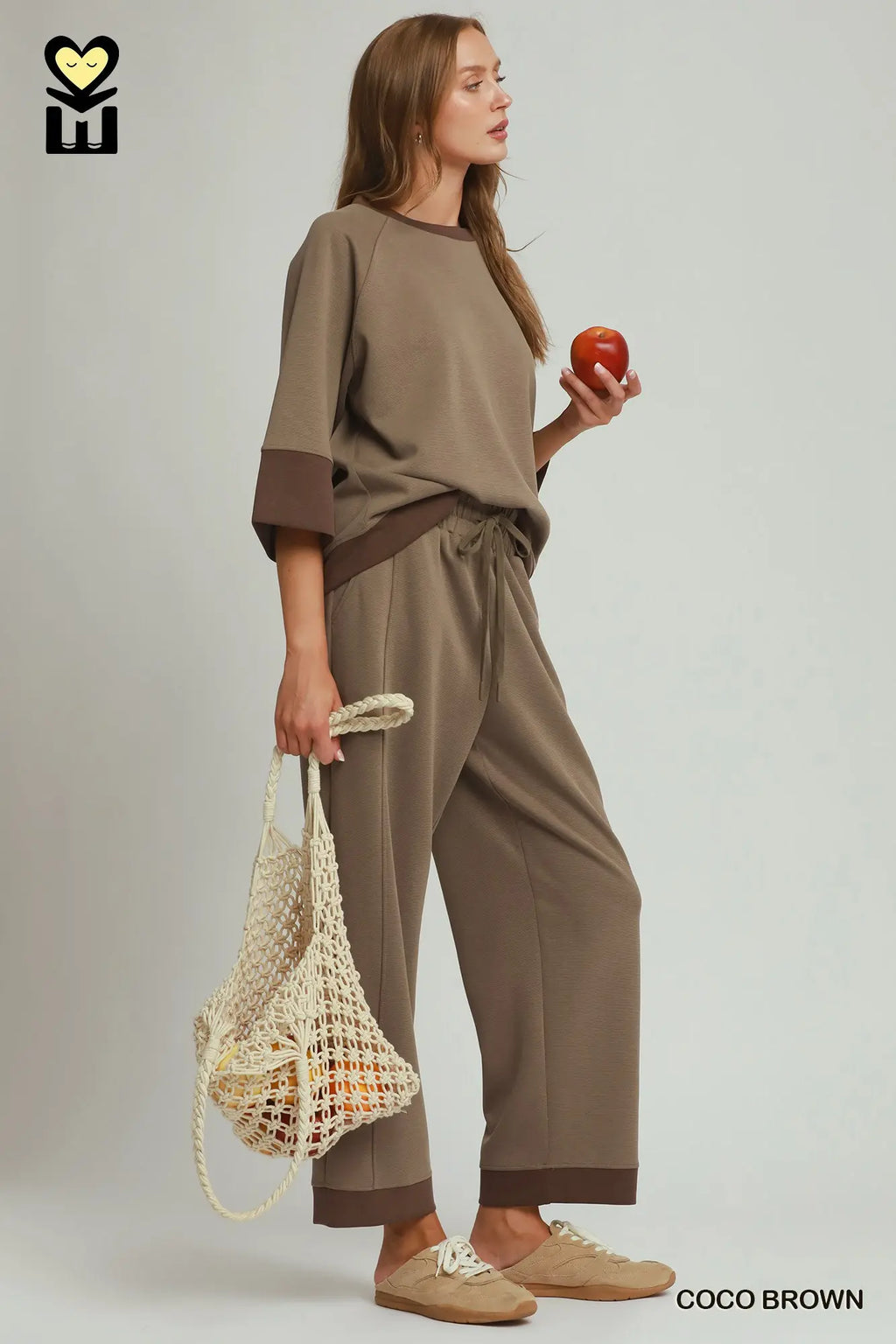 Woman in a beige outfit holding an apple and a reusable bag on a plain background