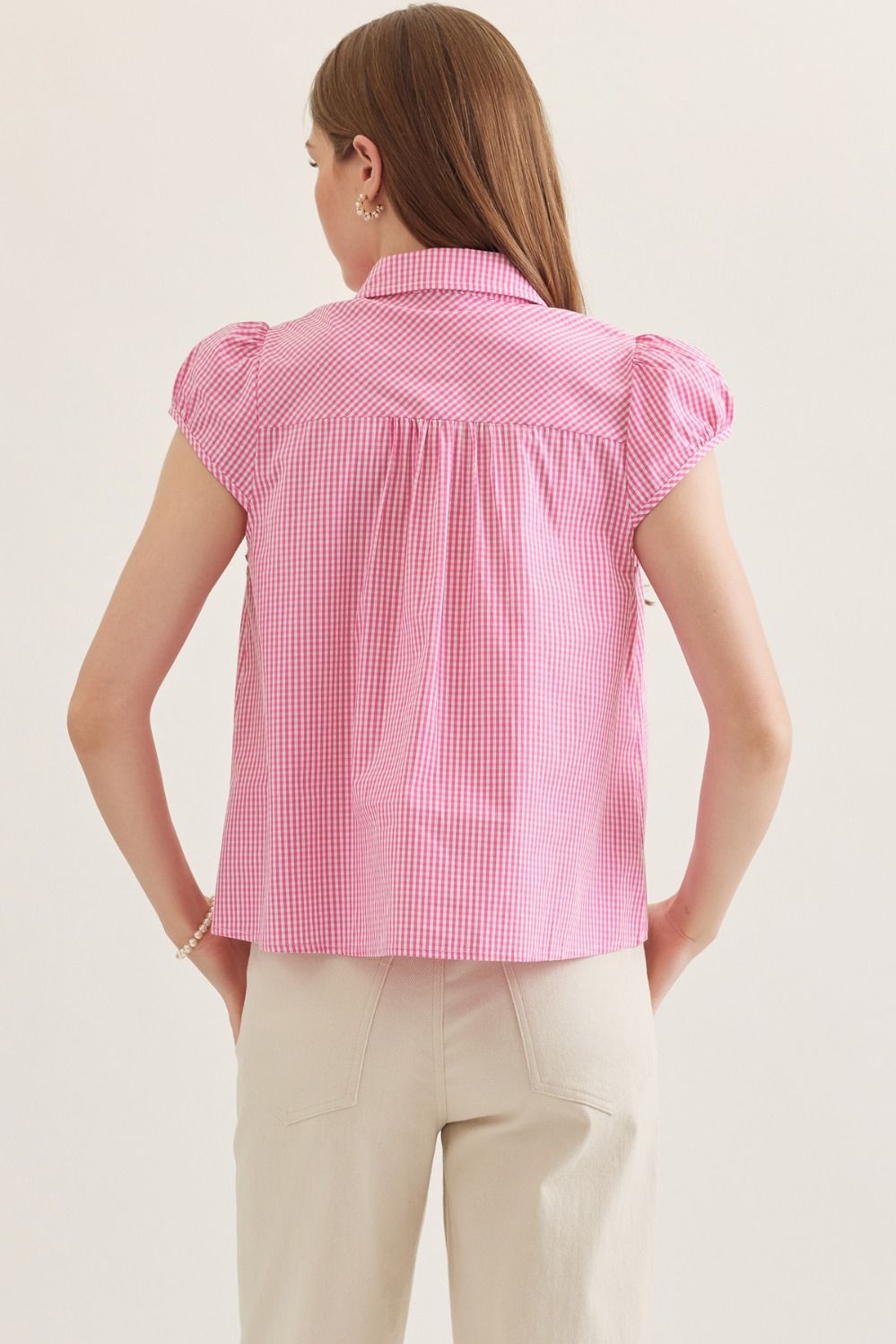 Woman wearing a pink checkered blouse with ruffled sleeves on a light background