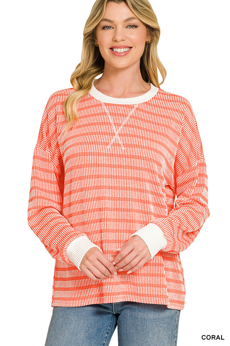 A woman wearing a coral and white horizontally striped long-sleeve knit top with white ribbed cuffs and collar, paired with blue jeans, against a plain white background.