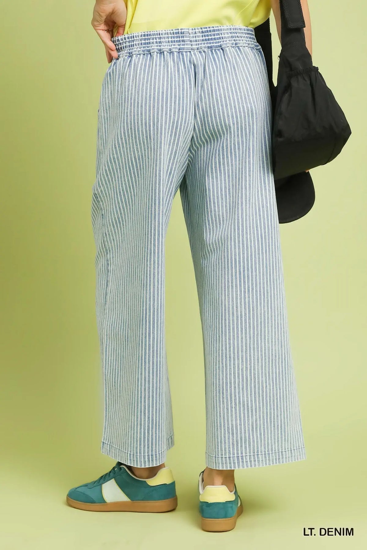 Person wearing light blue and white striped pants with a black bag on a yellow background