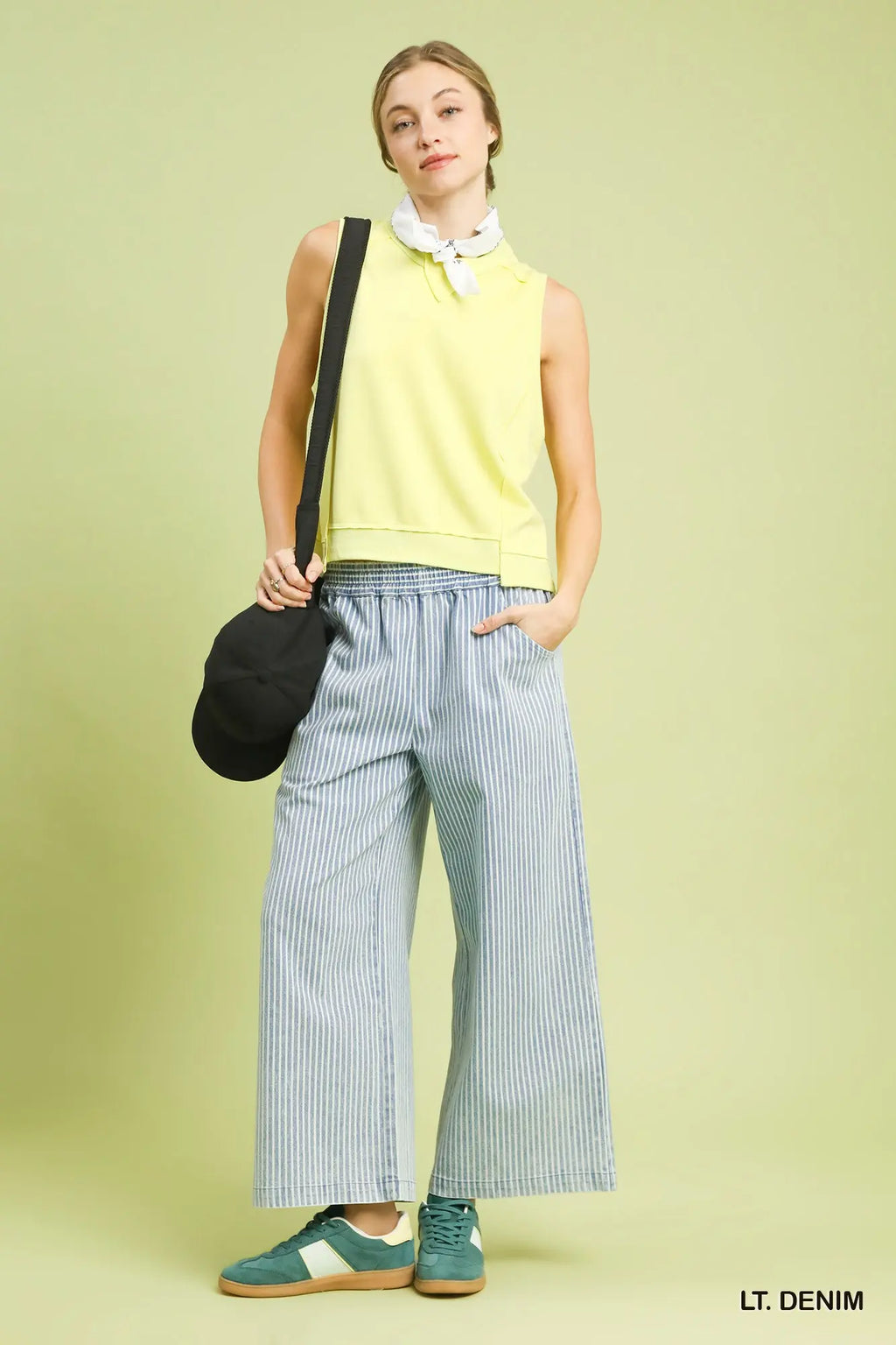 Woman wearing a yellow sleeveless top and light blue striped pants against a light green background