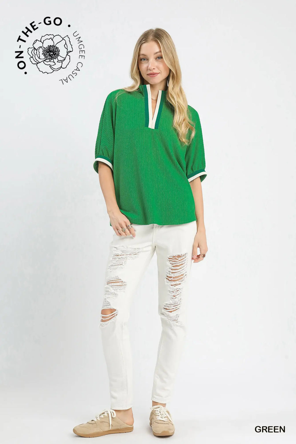 A woman modeling a green short-sleeve top with white trim and white distressed jeans, standing against a light gray studio background. The On-The-Go Lime Casual logo appears in the top left, and the word GREEN appears in the bottom right.