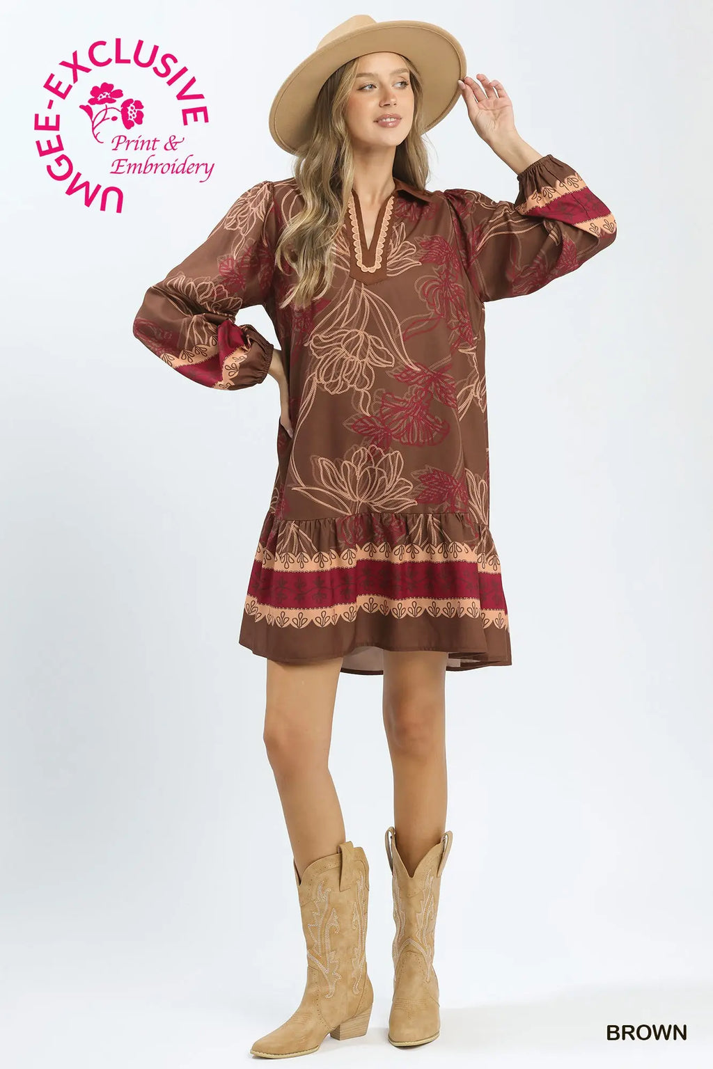A woman modeling a brown bohemian-style embroidered dress with floral patterns and red accents, paired with a tan hat and cowboy boots, on a white studio background.