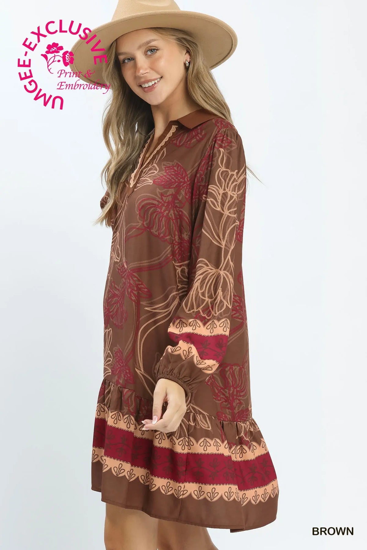 A woman wearing a brown long-sleeve dress with red and beige floral embroidery, a matching brown hat, and a beige background. A pink 'UNBEZCLIED' logo is visible in the top left, and the word 'BROWN' is in the bottom right corner.