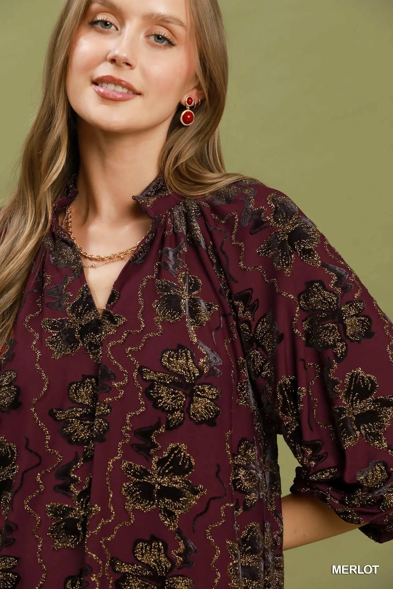 Woman wearing a maroon blouse with floral patterns against a green background