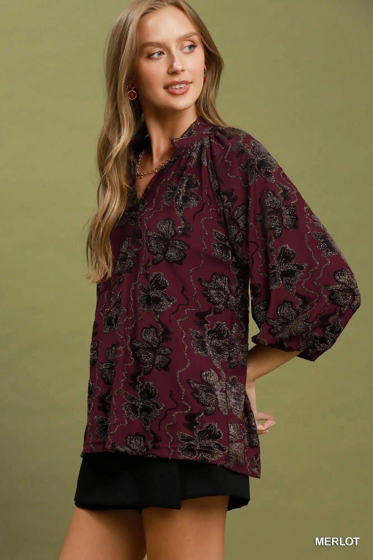 Woman wearing a maroon floral blouse against a green background